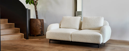 Koselig, moderne tosetersofa med myke puter på en slank metallramme, ledsaget av en stilren plantekasse og minimalistisk dekor.