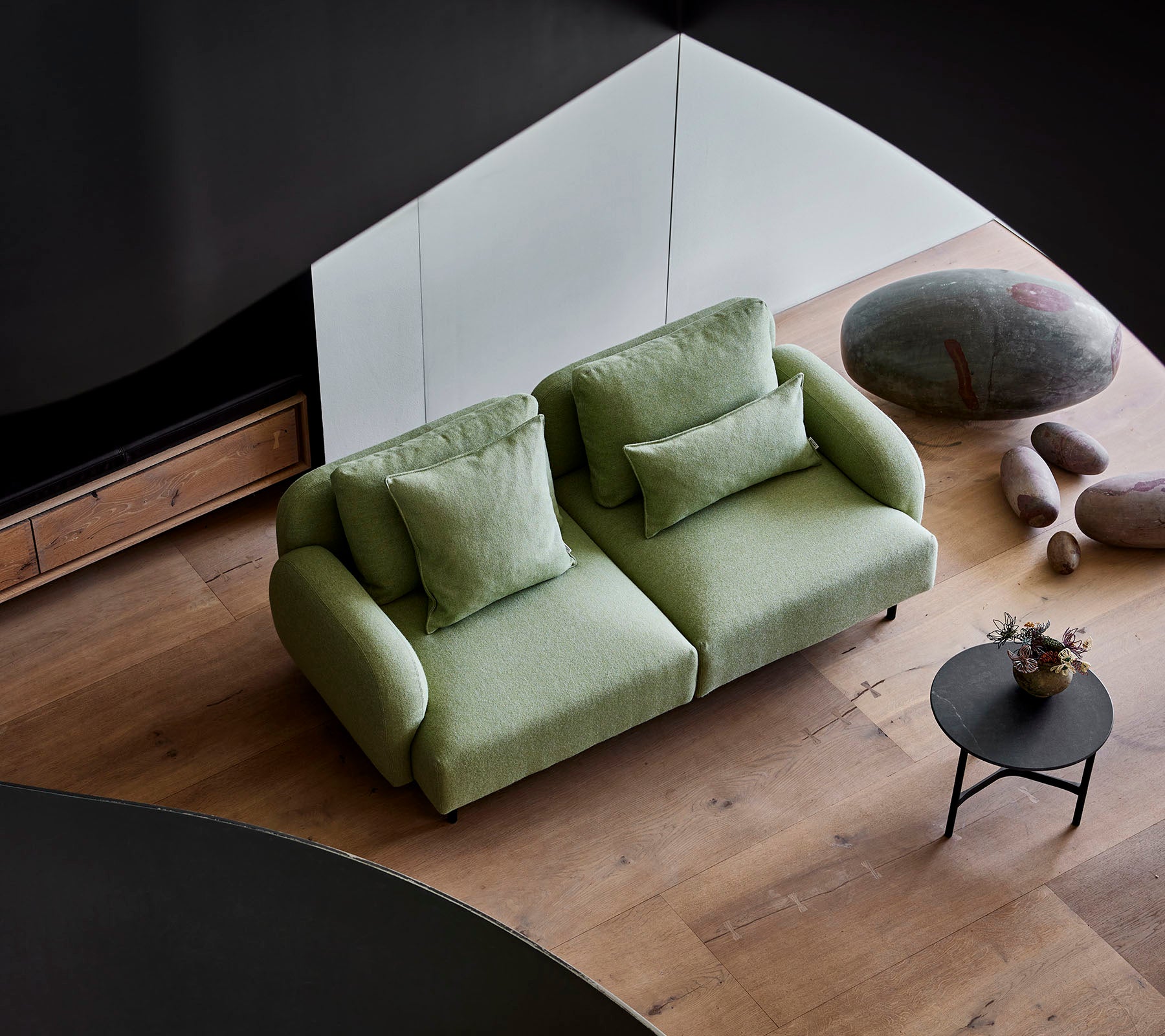 Stilig grønn sofa med deilige puter ved et lite rundt bord, mot en moderne bakgrunn med tregulv og glatte steiner.