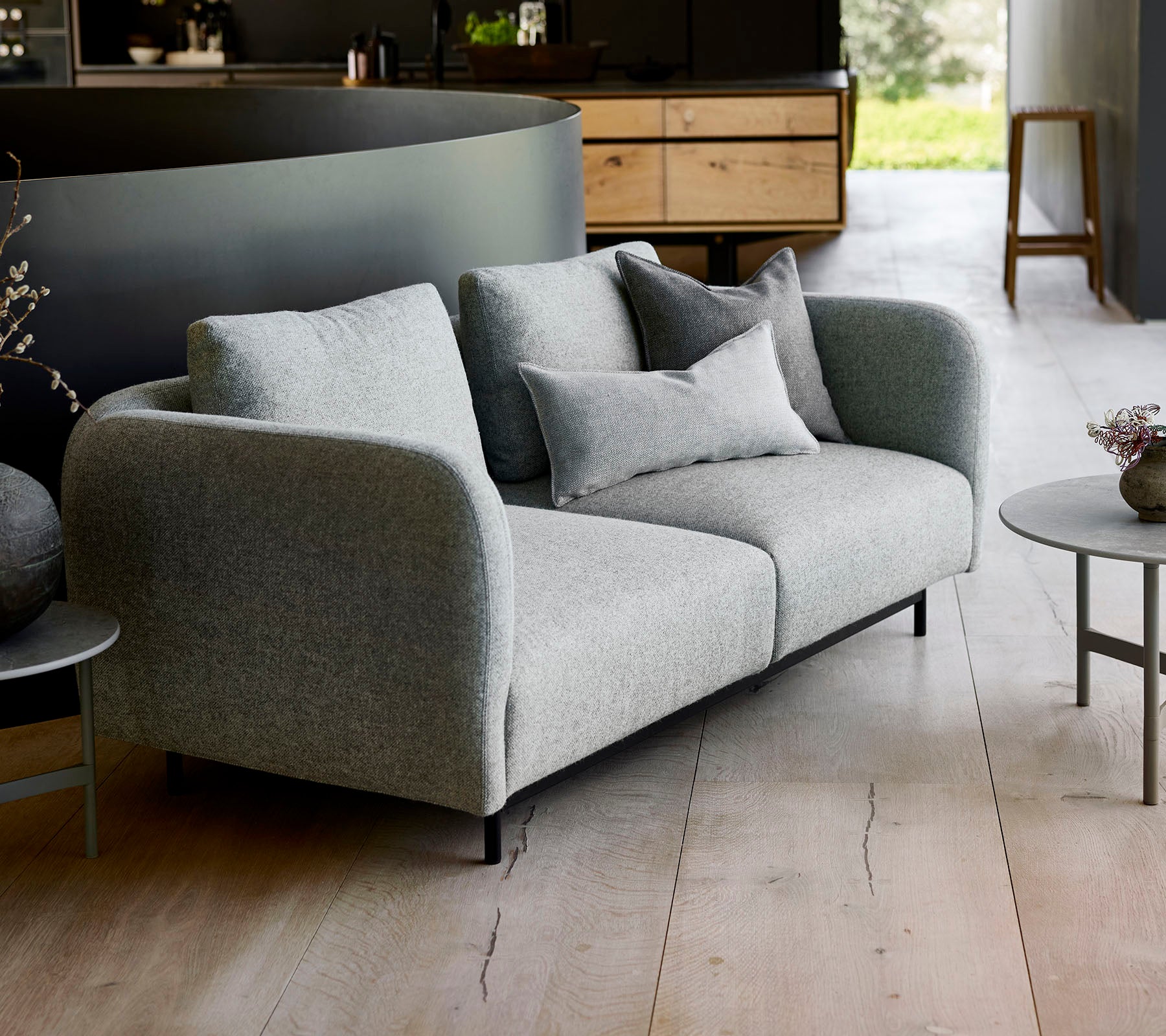 Moderne grå sofa med myke puter, kombinert med et lite rundt bord, satt mot en minimalistisk bakgrunn.