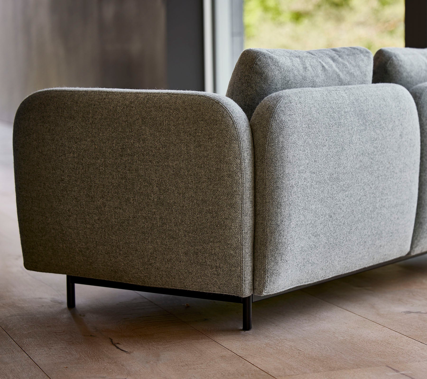 En moderne grå polstret sofa med avrundede kanter og slanke sorte ben som viser et minimalistisk design.