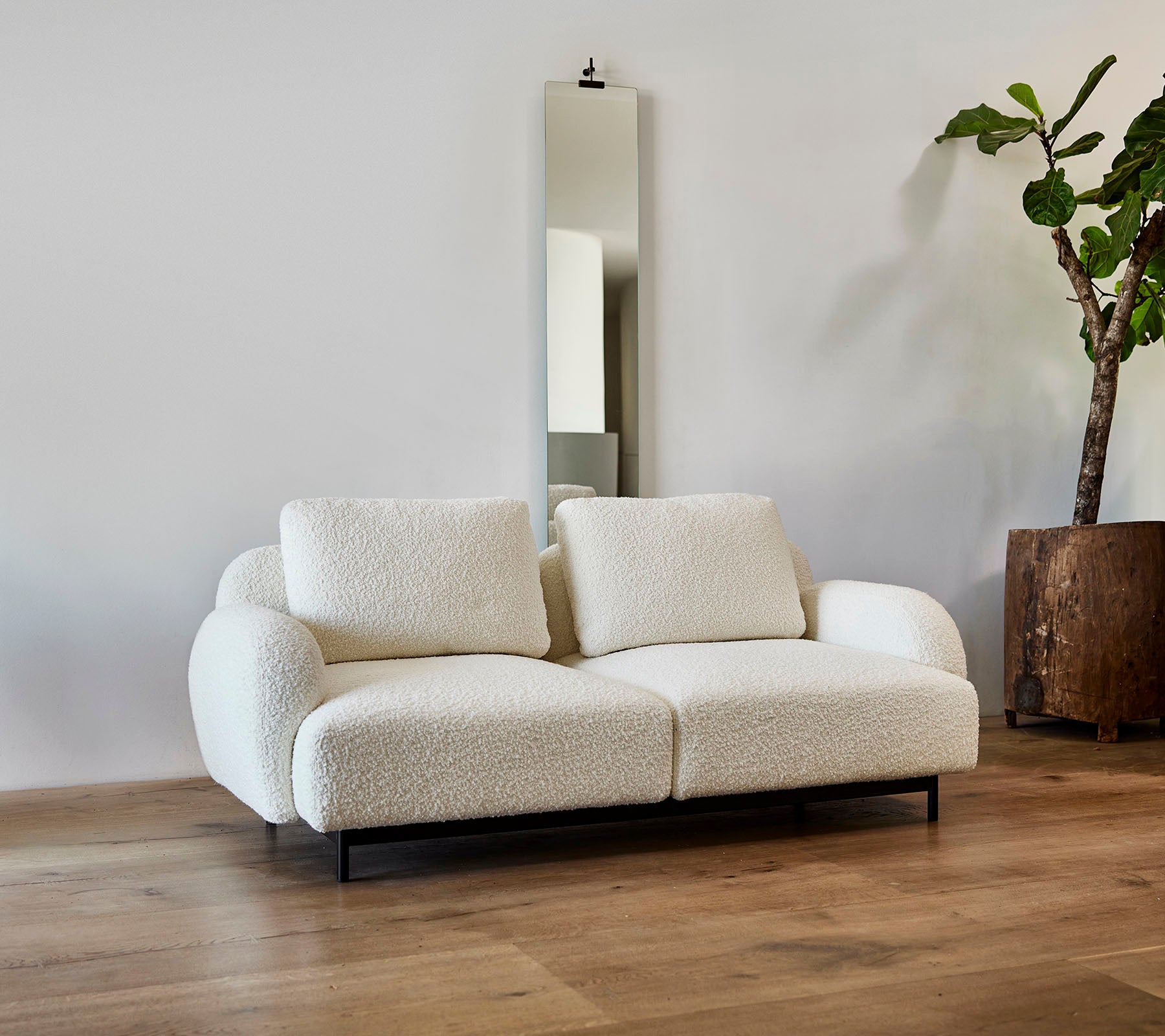 En stilfull hvit sofa med myke puter, kombinert med et stort speil og en potteplante i et moderne miljø.