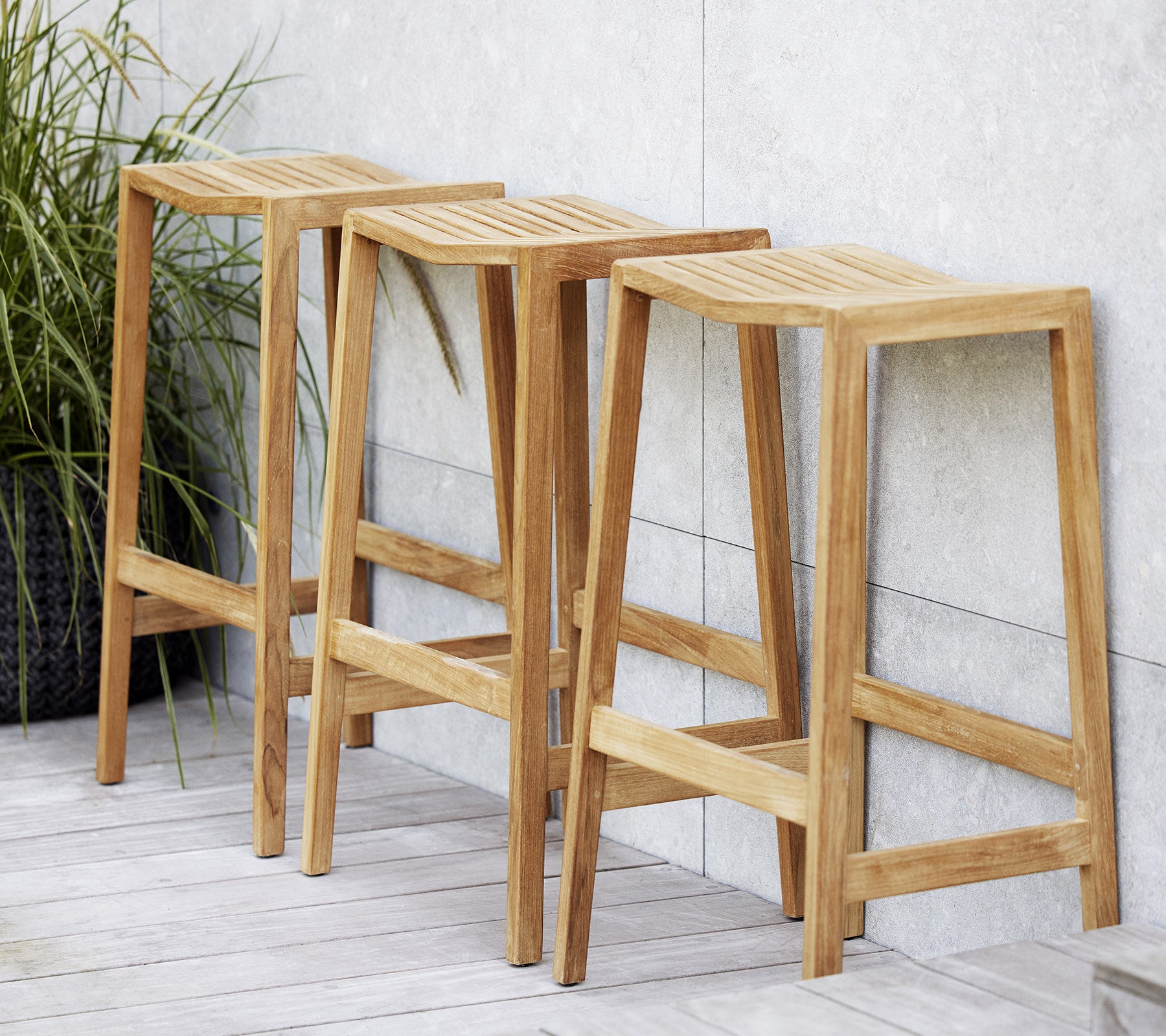 Tre treflip-barstoler med revne seter, med et minimalistisk design og rene linjer, plassert ved siden av en dekorativ plante.