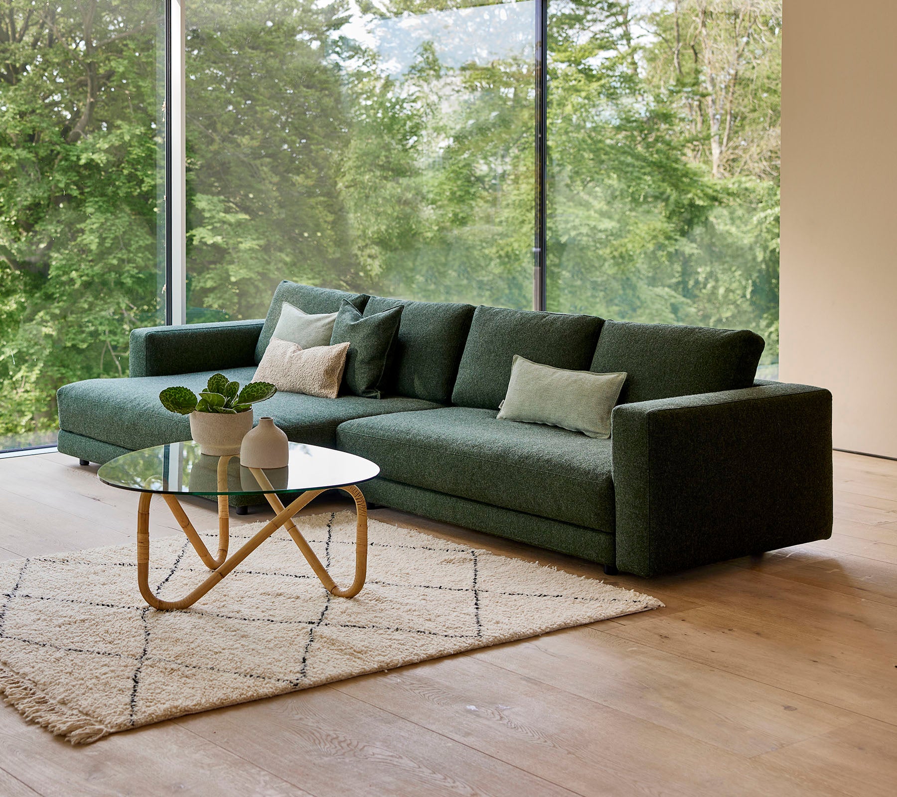 En moderne grønn sofa med puter, akkompagnert av et rundt kaffebord og et dekorativt teppe, mot en bakgrunn av grønt.