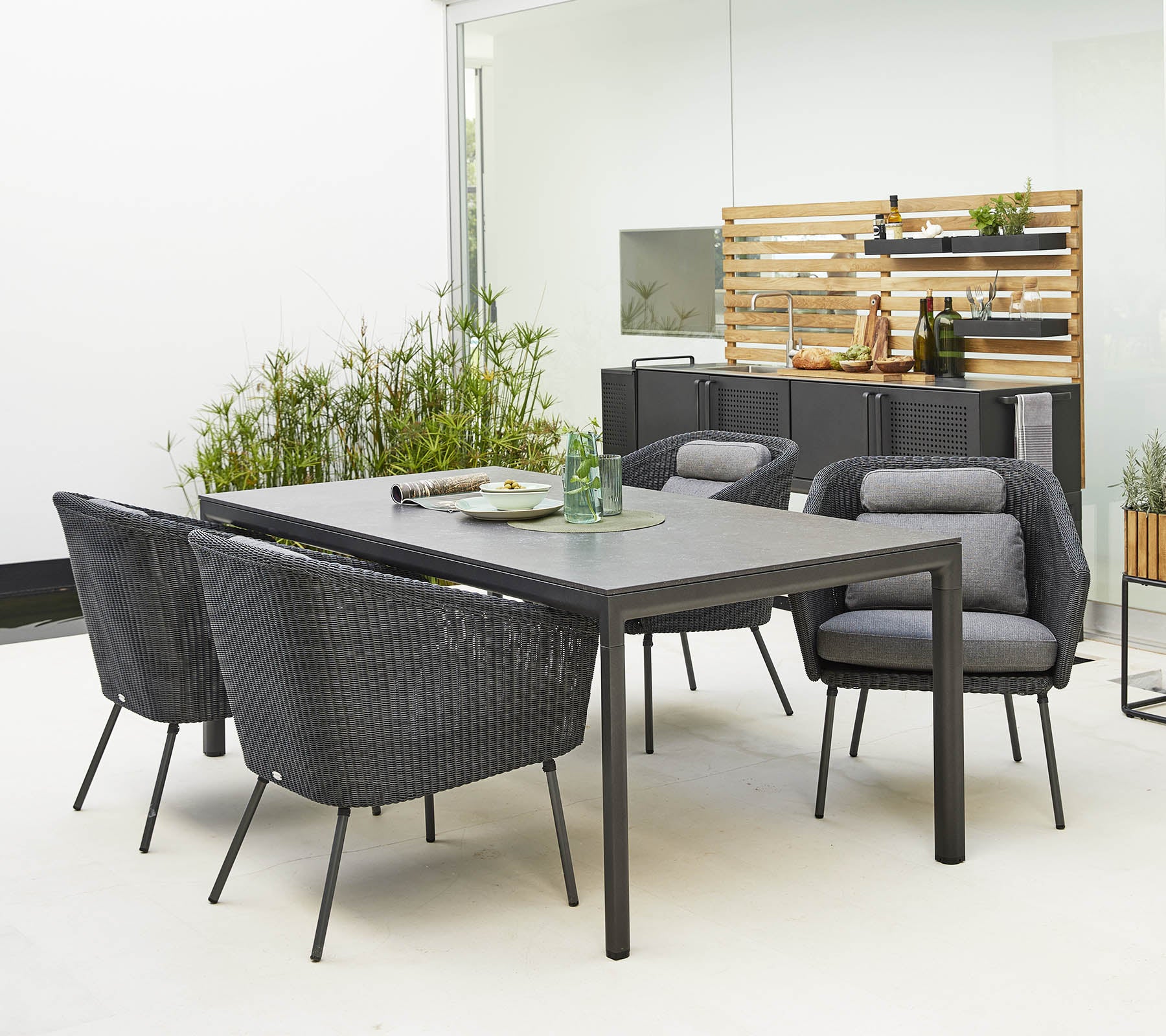 Stilig utendørs spisegruppe med et slankt bord og komfortable, moderne stoler omgitt av dekorativ grøntområder.