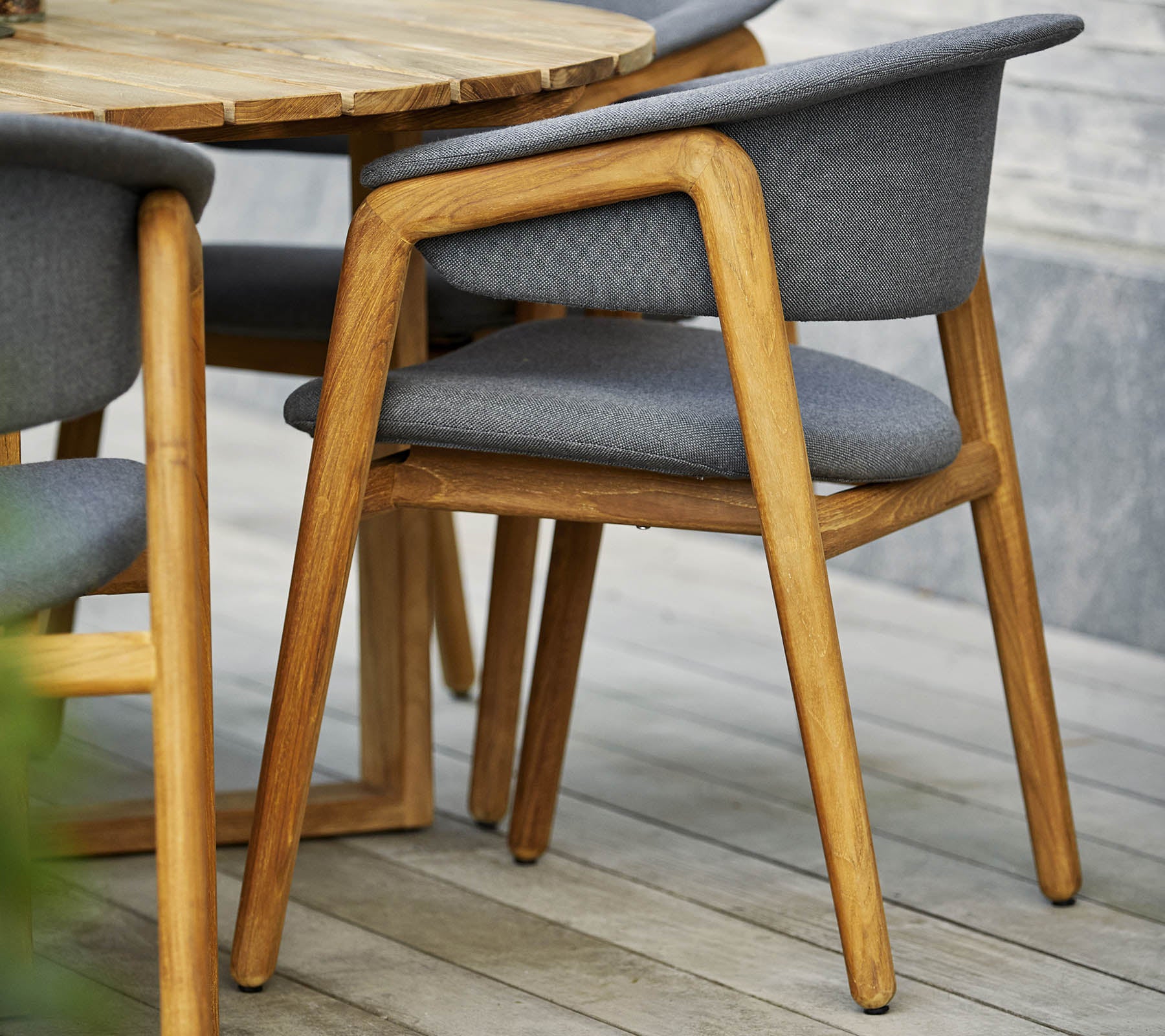 Stilig trestol med grå polstret sete og ryggstøtte, kombinert med et rundt bord i moderne design.