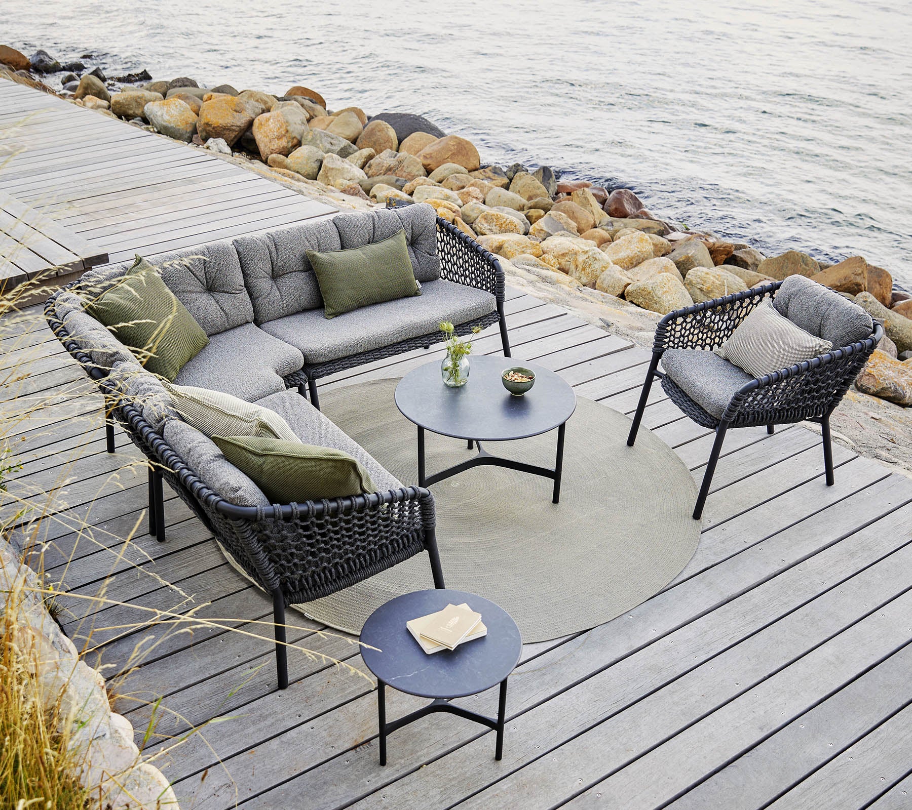 En stilig ute sittearrangement med en modulsofa og stoler med grå puter, et rundt bord og dekorative detaljer.
