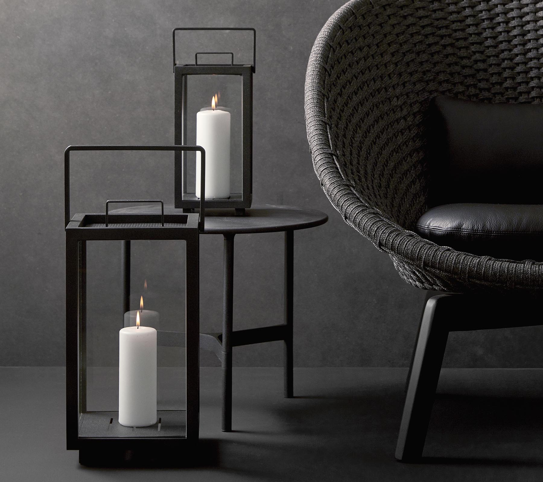To stilige lampe med hvite lys, akkompagnert av en moderne, teksturert stol på et minimalistisk bord mot en mørk bakgrunn.