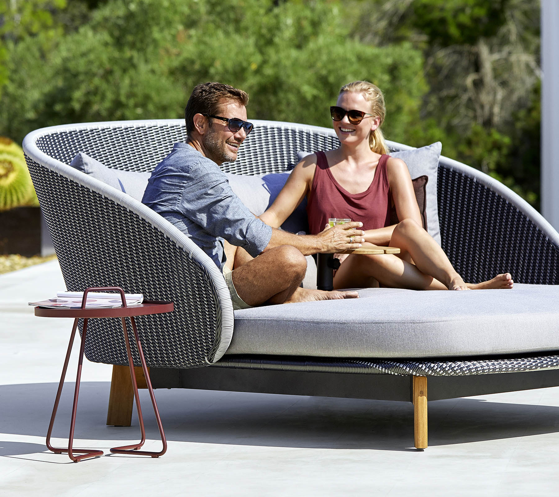 Et par nyter et koselig øyeblikk sammen på en stilfull, buet ute-sofa med et sidebord i nærheten.