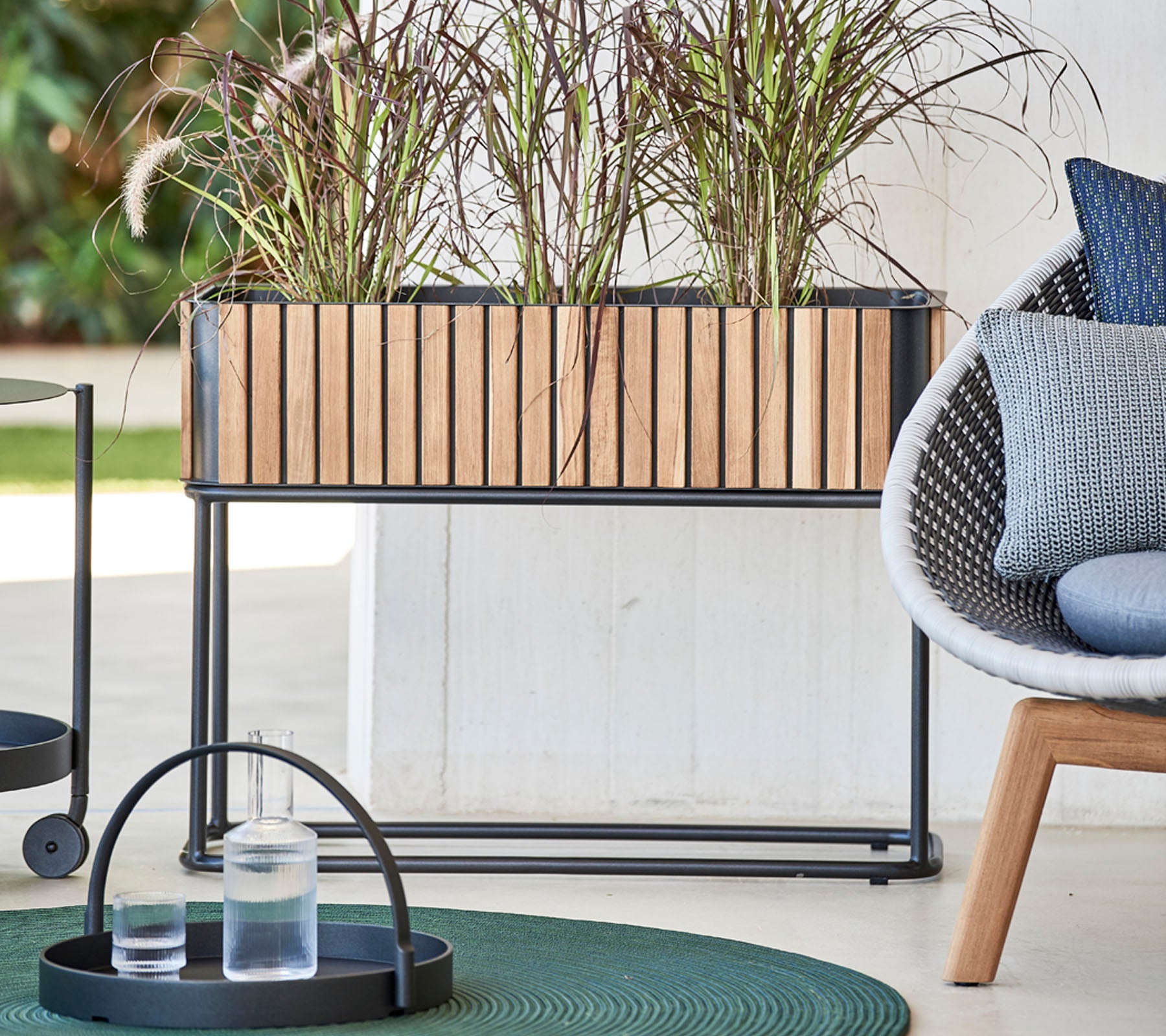 Trekasse med dekorative planter, ledsaget av et rundt brett med glass og en moderne stol med myke puter.