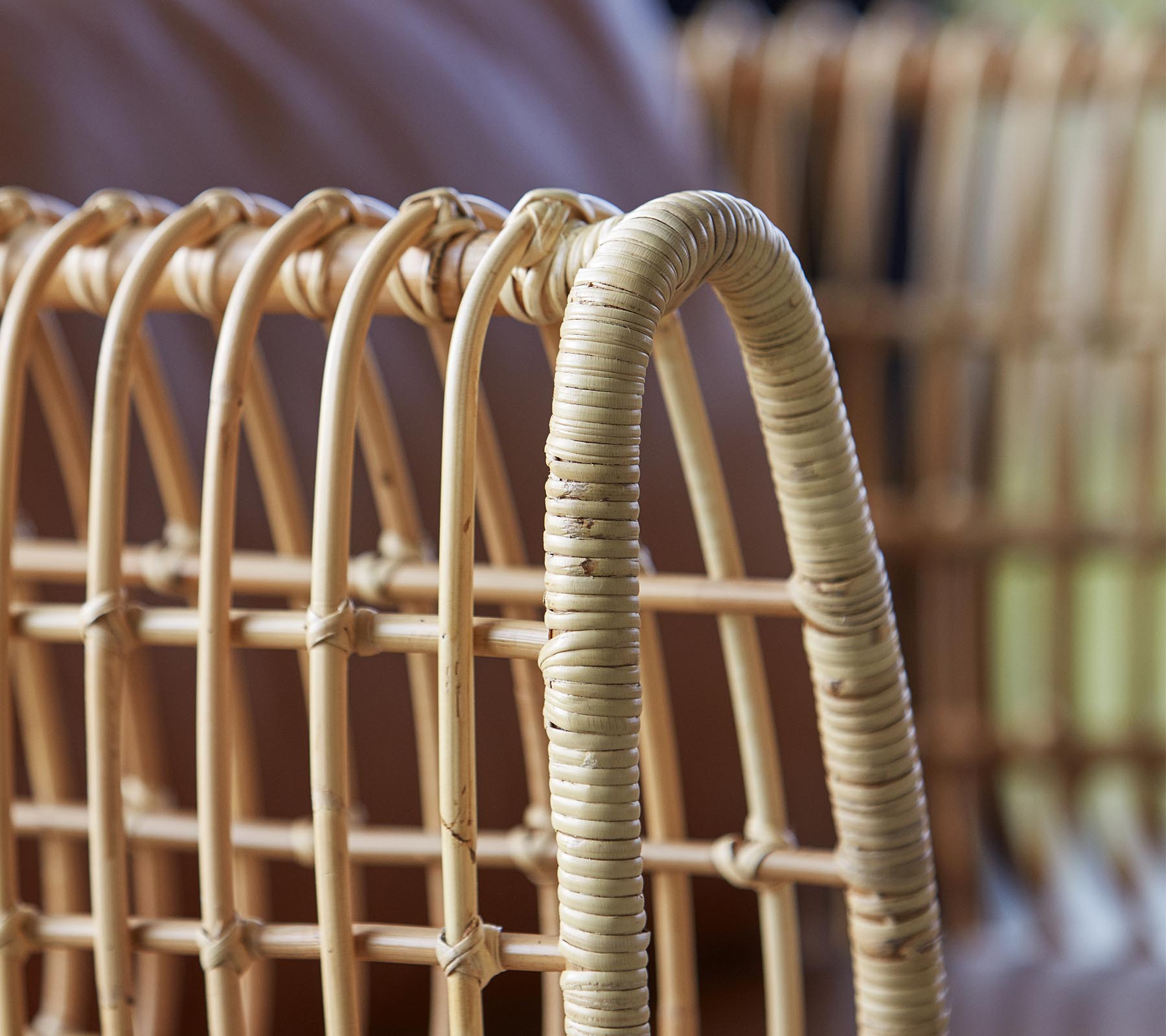 Nærbilde av en vevd rattanstol med buede linjer og en naturlig finish som fremhever håndverkskvaliteten og designet.