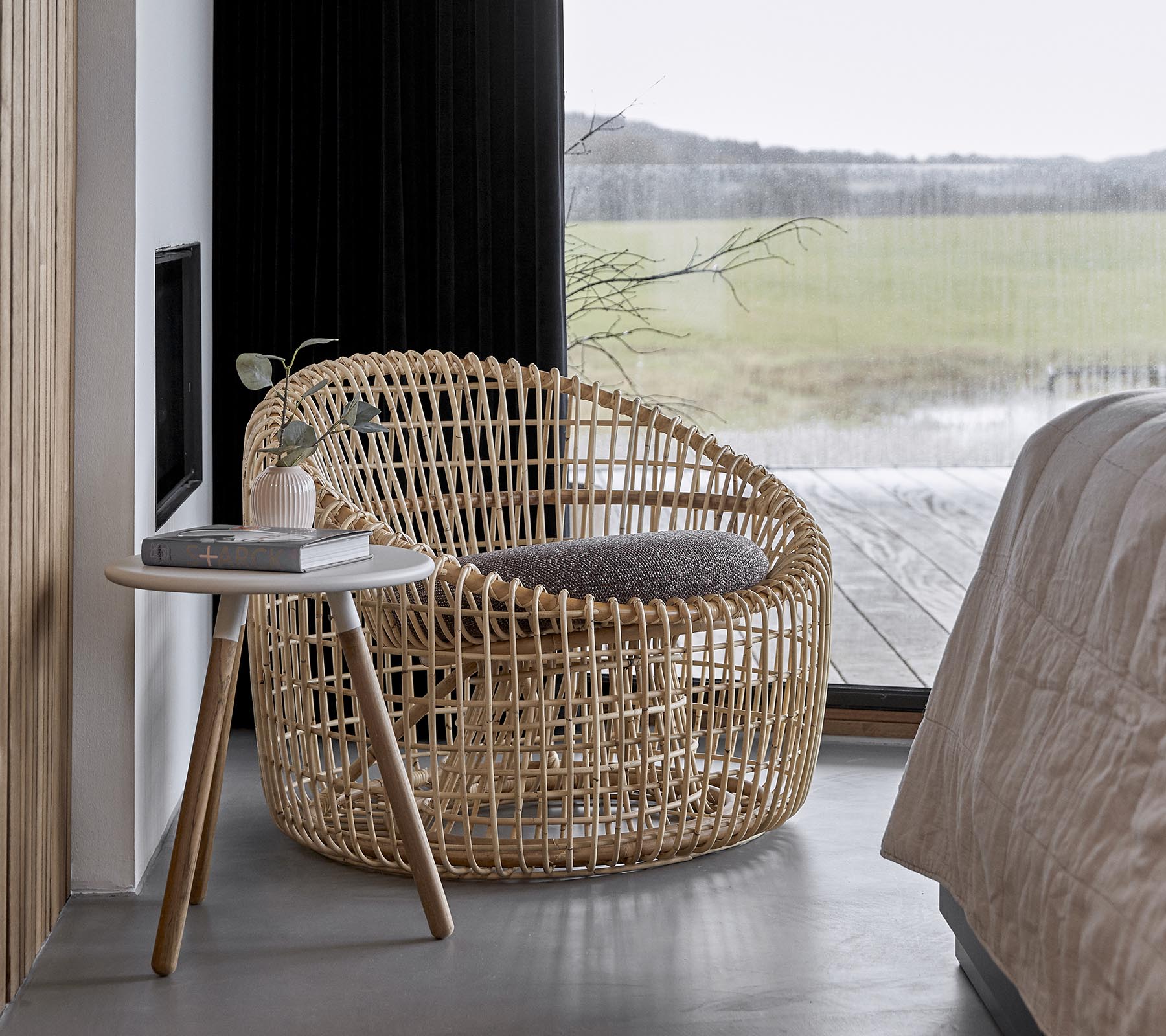 En stilfull vevd stol kombinert med et lite sidebord, plassert i et fredelig miljø med store vinduer som slipper inn naturlig lys.