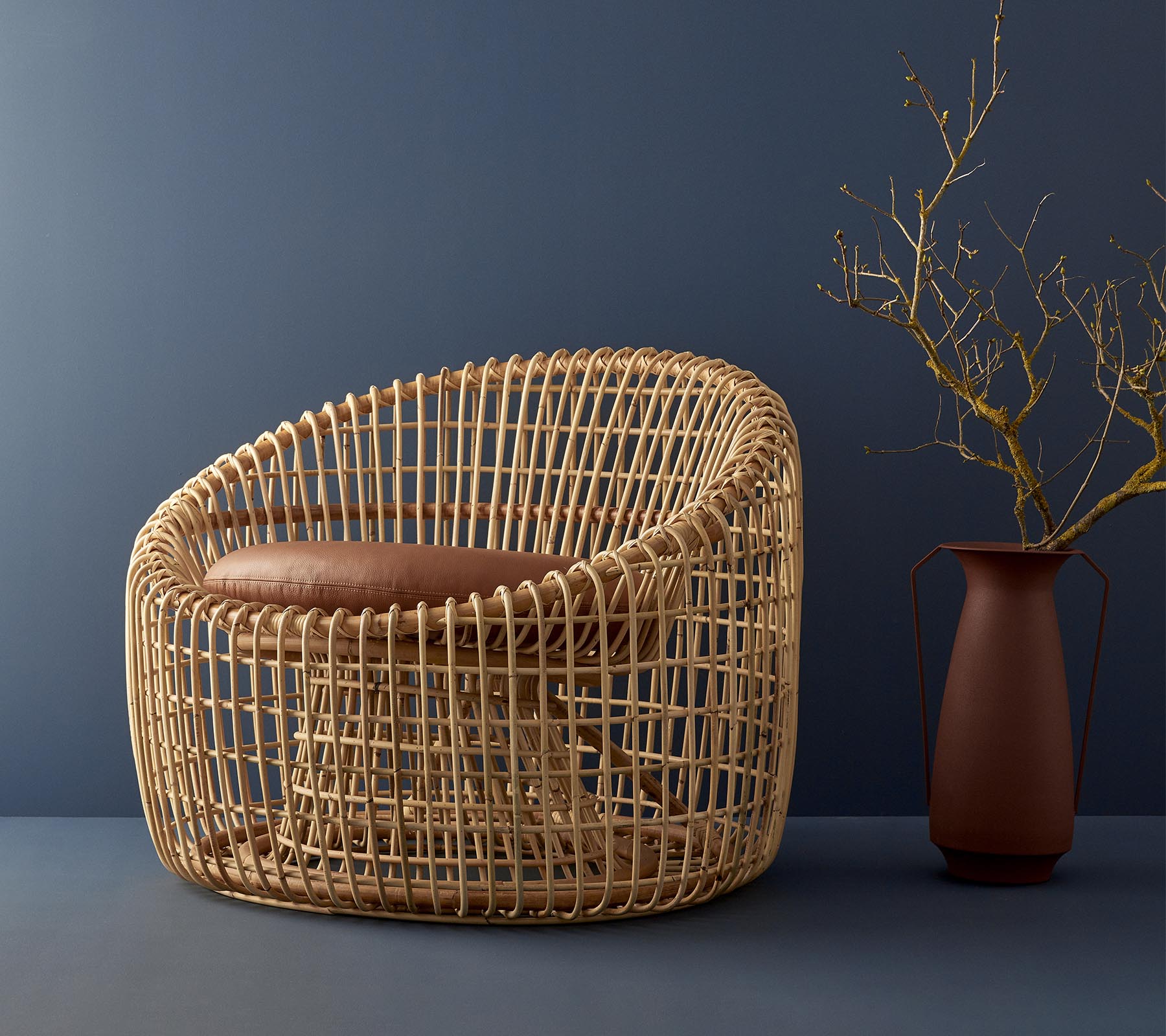 Moderne kurvstol med avrundet design, med en polstret sete og supplerende med en enkel vase med en kvist.