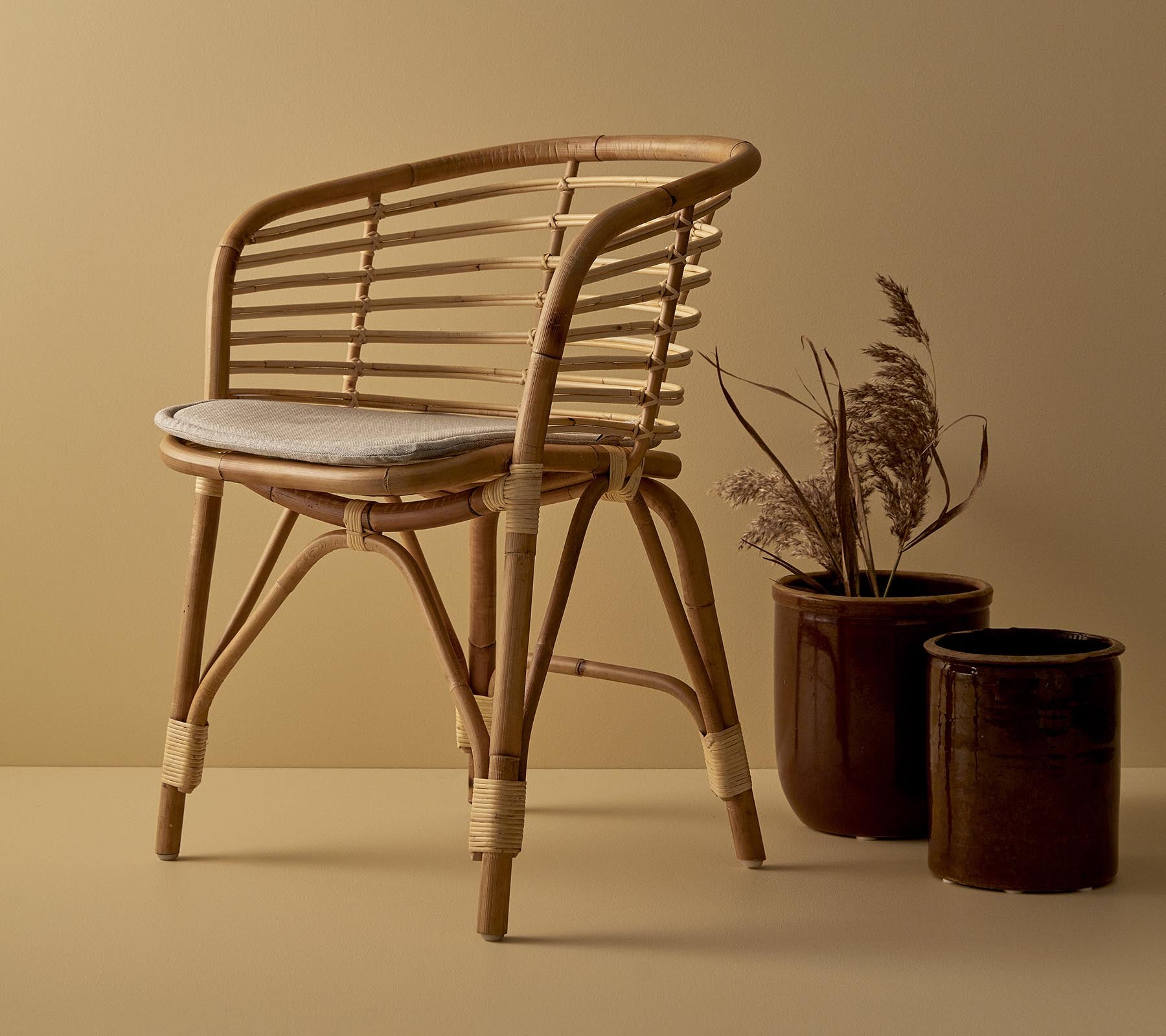 En stilfull rattan stol med polstret sete, ledsaget av to dekorative plantekasser med tørkede planter.