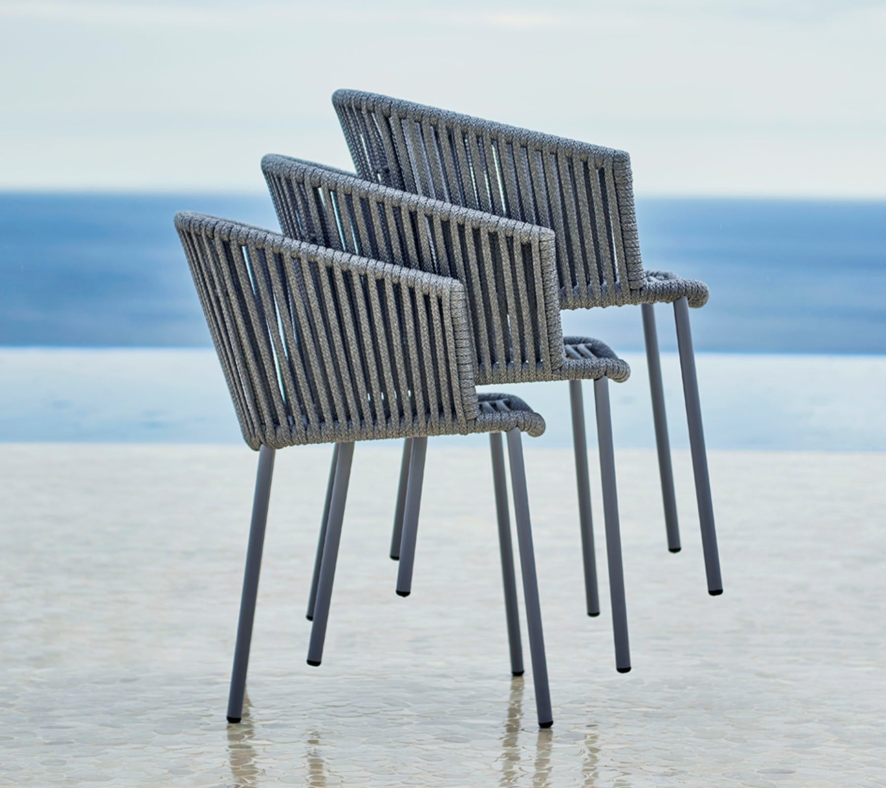 Tre moderne stoler med et stilrent design, med ribbet rygg og armlener, plassert ved siden av en fredelig vannutsikt.