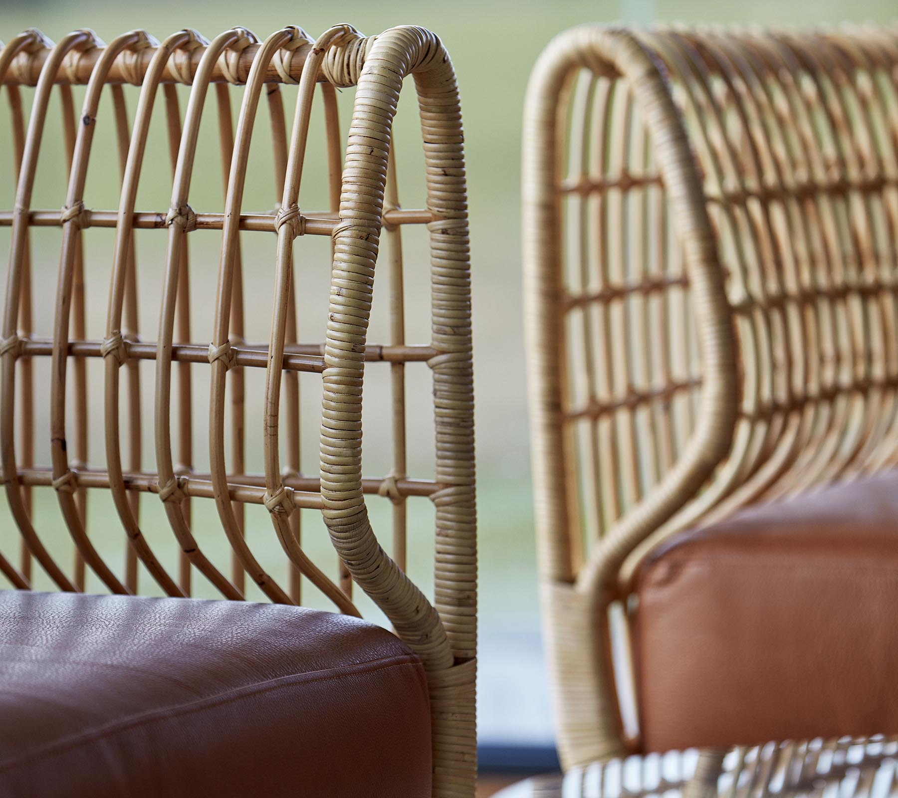 To stilige stoler med flettede rottingsriper og glatte skinnseter, som viser en moderne designestetikk.