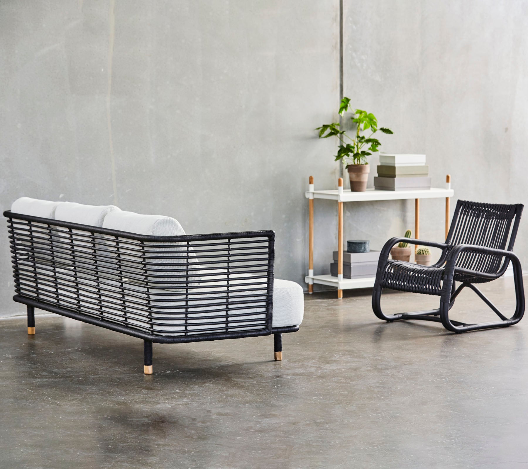 En moderne sitteordning med en stilfull svart rammesofa med hvite puter og en matchende gyngestol, aksentuert av grønne planter.