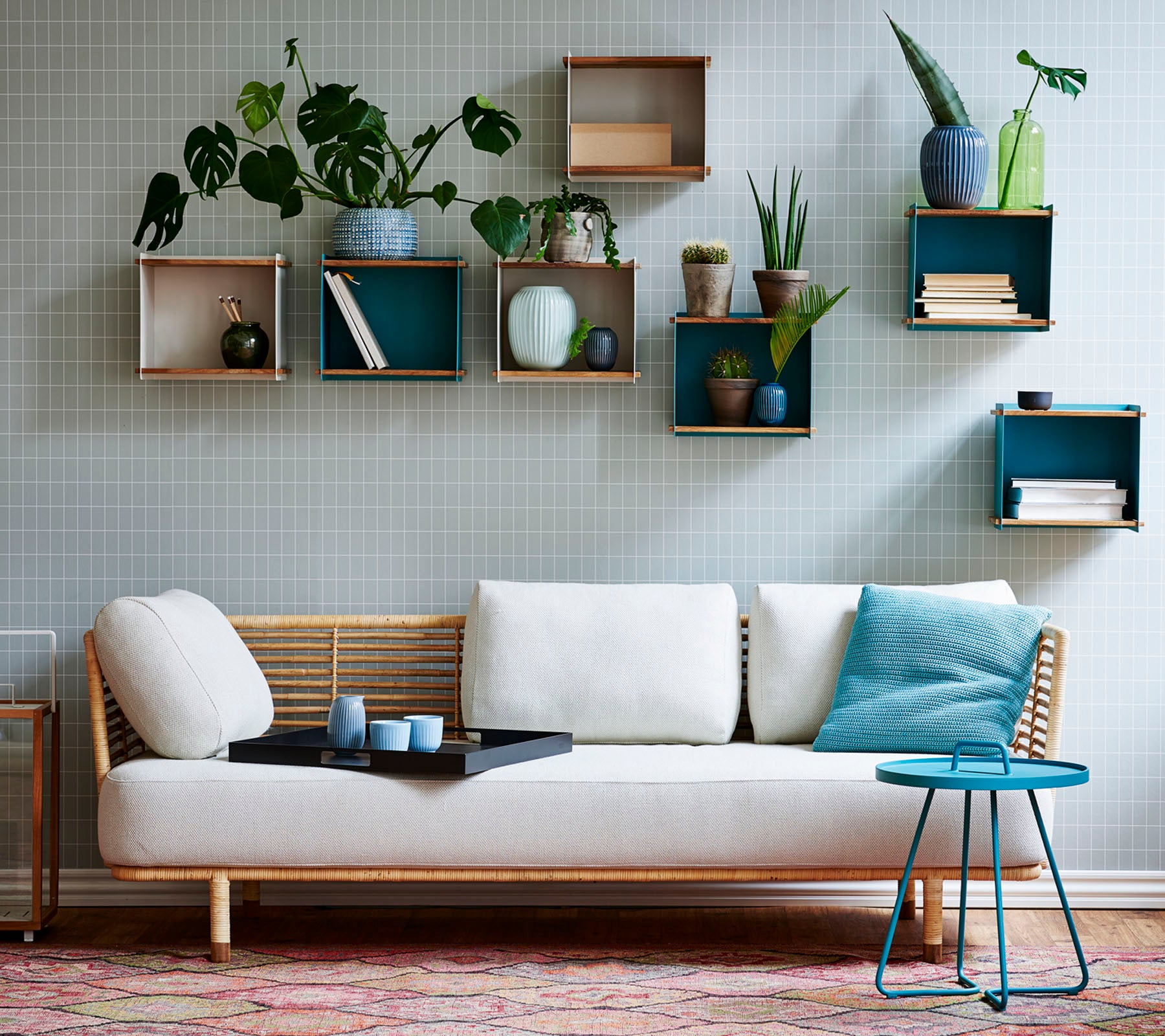 En stilfull sofa med en lett pute og et lite bord, pyntet med forskjellige potteplanter vist frem på geometriske hyller.