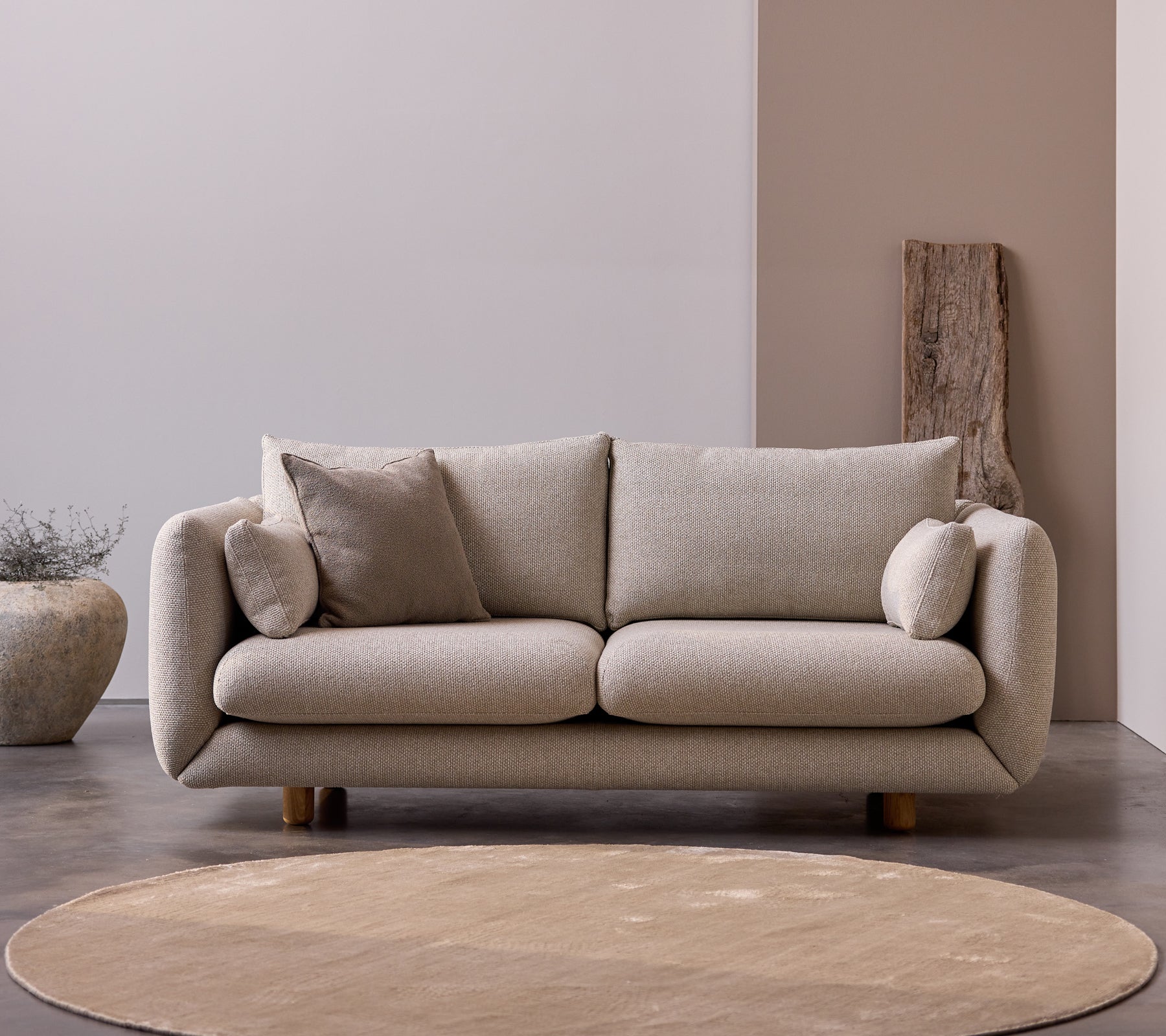 Bloom 2-seters sofa med teakbein i fargen Desert Sand, med myke puter og et mykt, minimalistisk design.