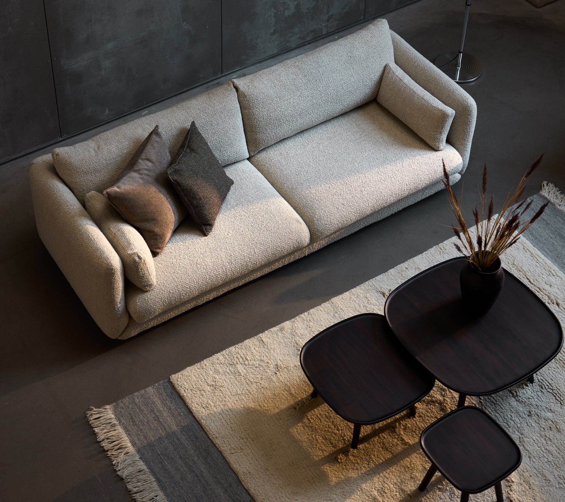 Stilig tresetersofa i sandfarge, supplert med tre størrelser av slanke svarte kaffebord og dekorative puter.