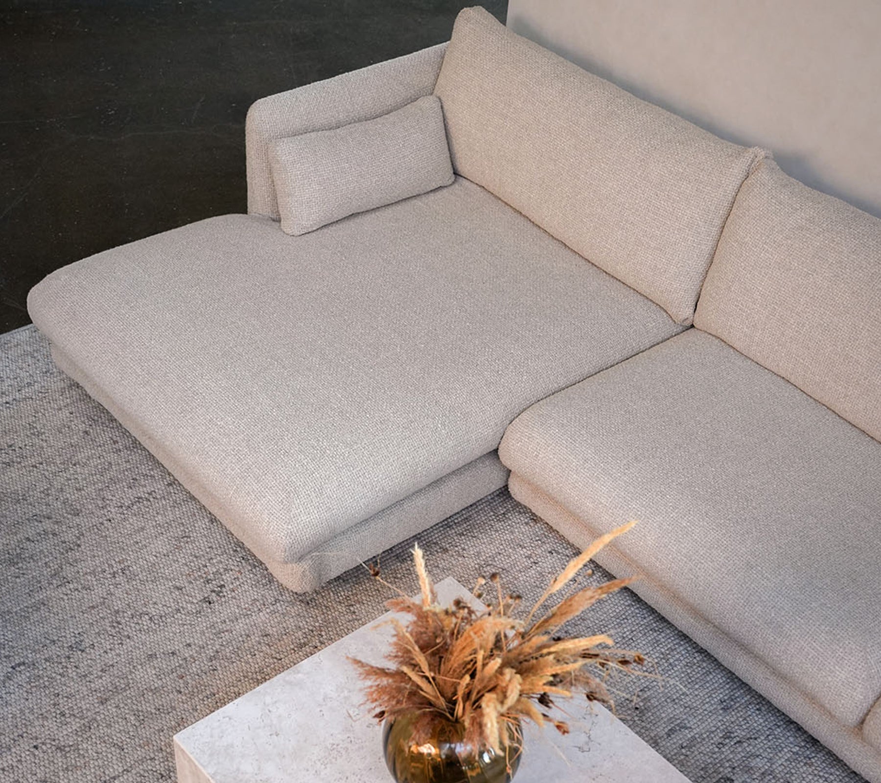 Moderne beige sofa med et hvitt bord og en dekorativ vase i en stilig loungeinnstilling.