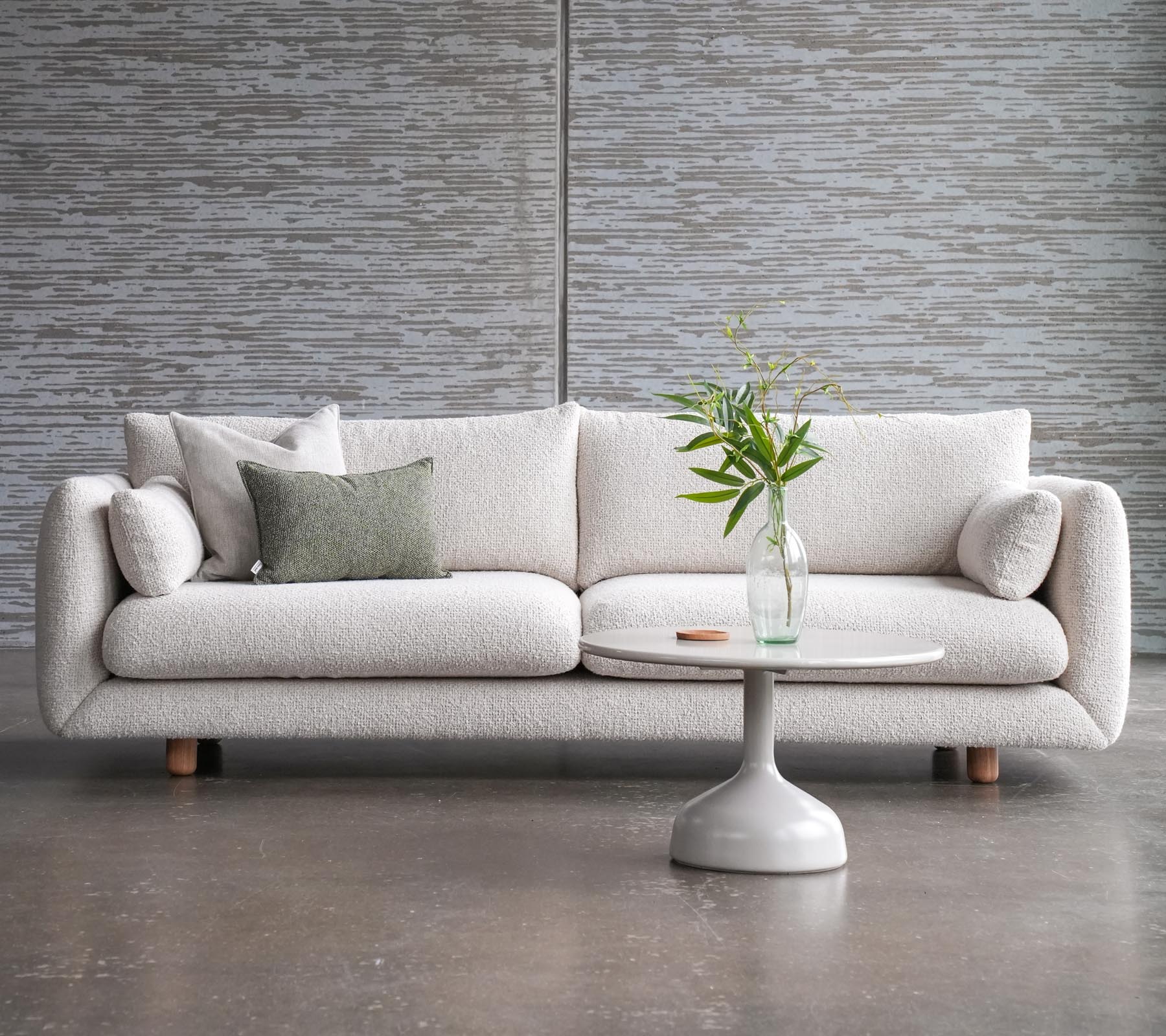 En stilfull sofa med puter ved siden av et Glaxe sofa bord med rund topp og elegante teakben, pyntet med en vase med blomster.