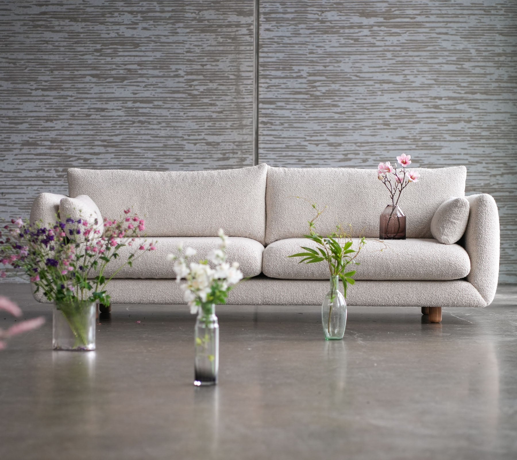 En lys sofa med teakbein, omgitt av blomster vaser, som viser en blanding av eleganse og Cane-line stil.