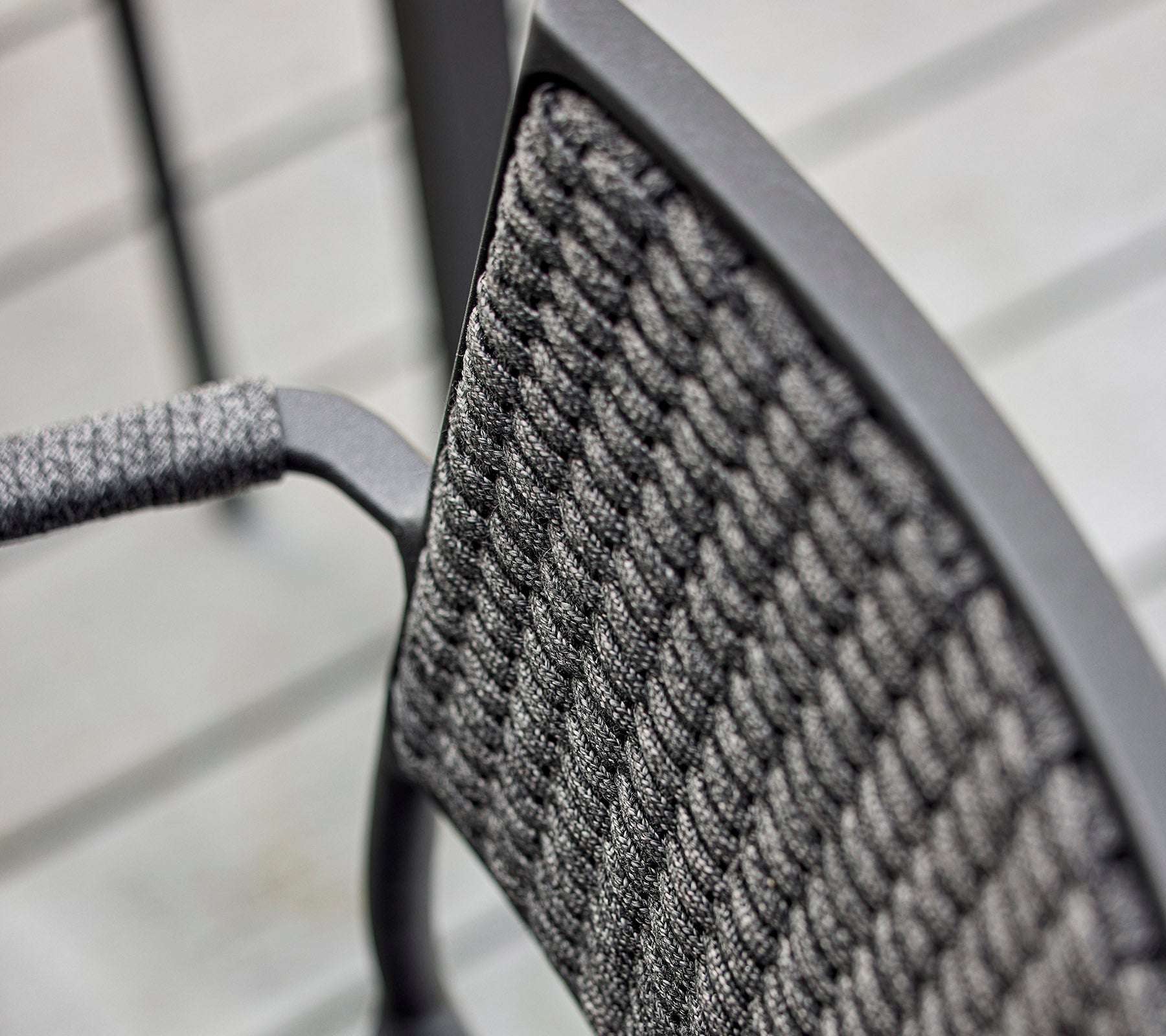 Nærbilde av en stolrygg med et teksturert vevd design og en slank metallramme, som fremhever moderne håndverk.