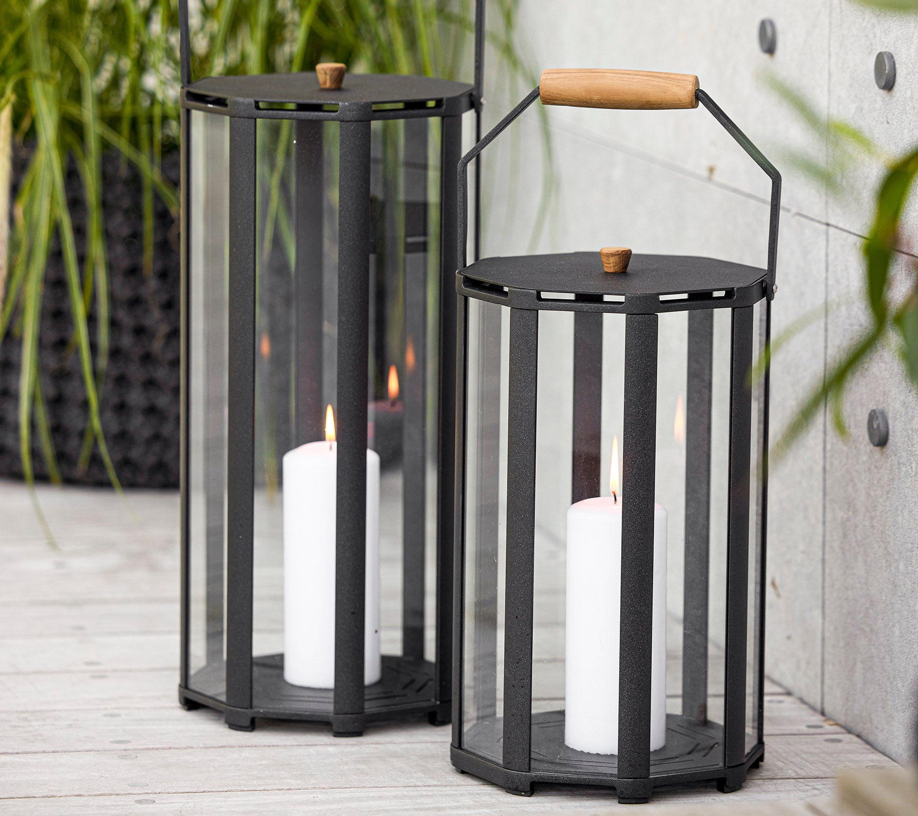 To stilige lanterner med moderne design, med glasspanler og et treskaft, som holder hvite stearinlys inni.