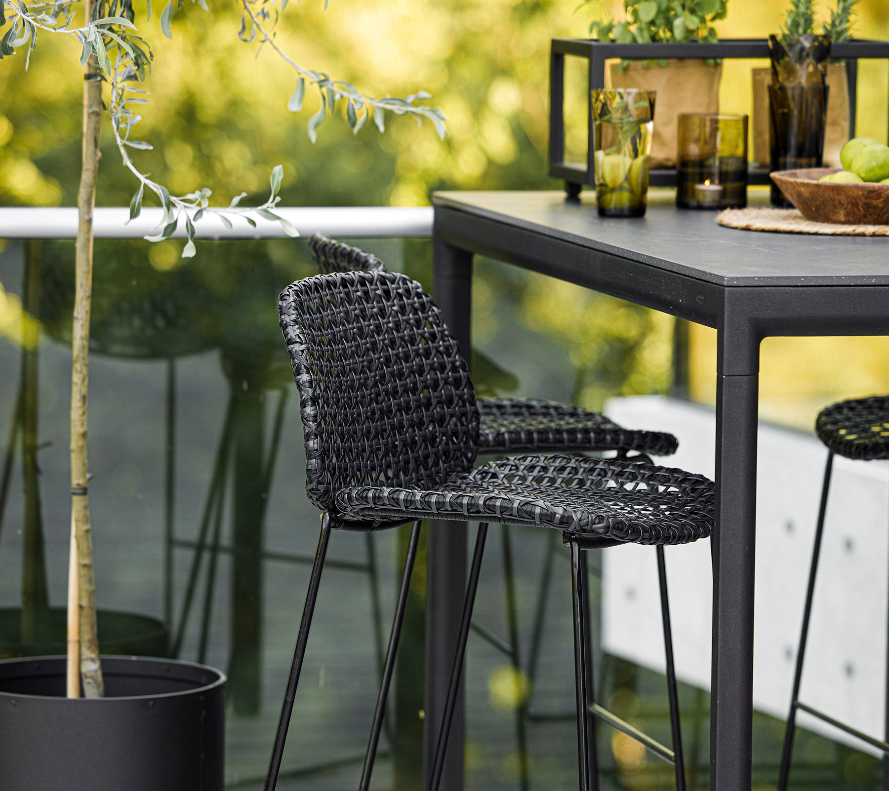 En stilfull svart vevd stol kombinert med et elegant bord, omgitt av dekorative planter og glassvarer, som skaper en moderne setting.