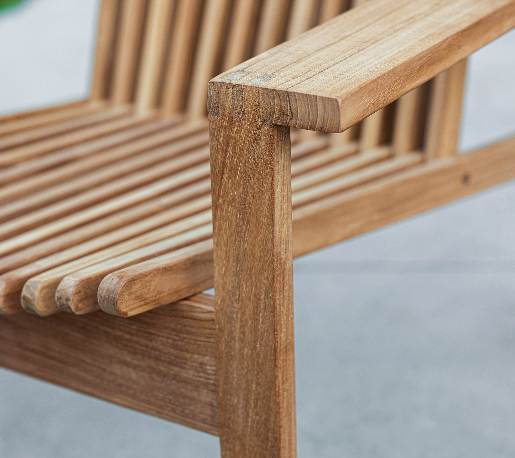 Nærbilde av en benk i tre med et lamell-design og en solid armlene, som viser naturlig treverk og håndverk.