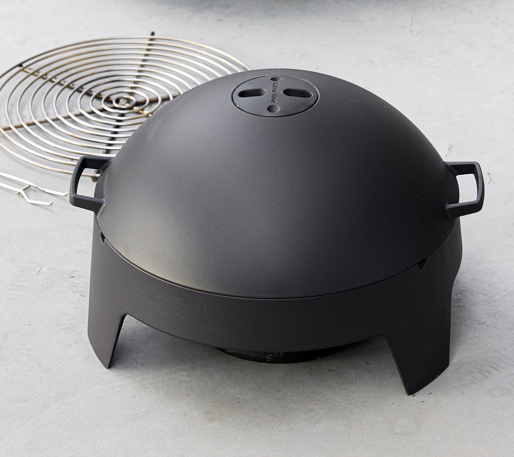 En slank svart matlagingsapparat med en kuppelform og håndtak, sammen med et sirkulært grillrist. Ideell for grilling og utendørs matlaging.