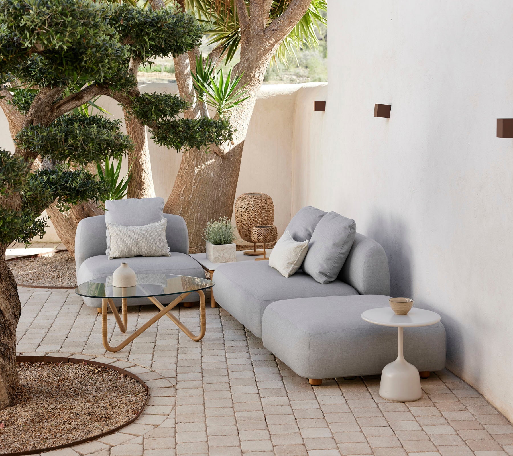 Moderne utendørs sittearrangement med en koselig sofa, aksentstol og stilfullt sidebord, omgitt av grøntområder og dekorative elementer.