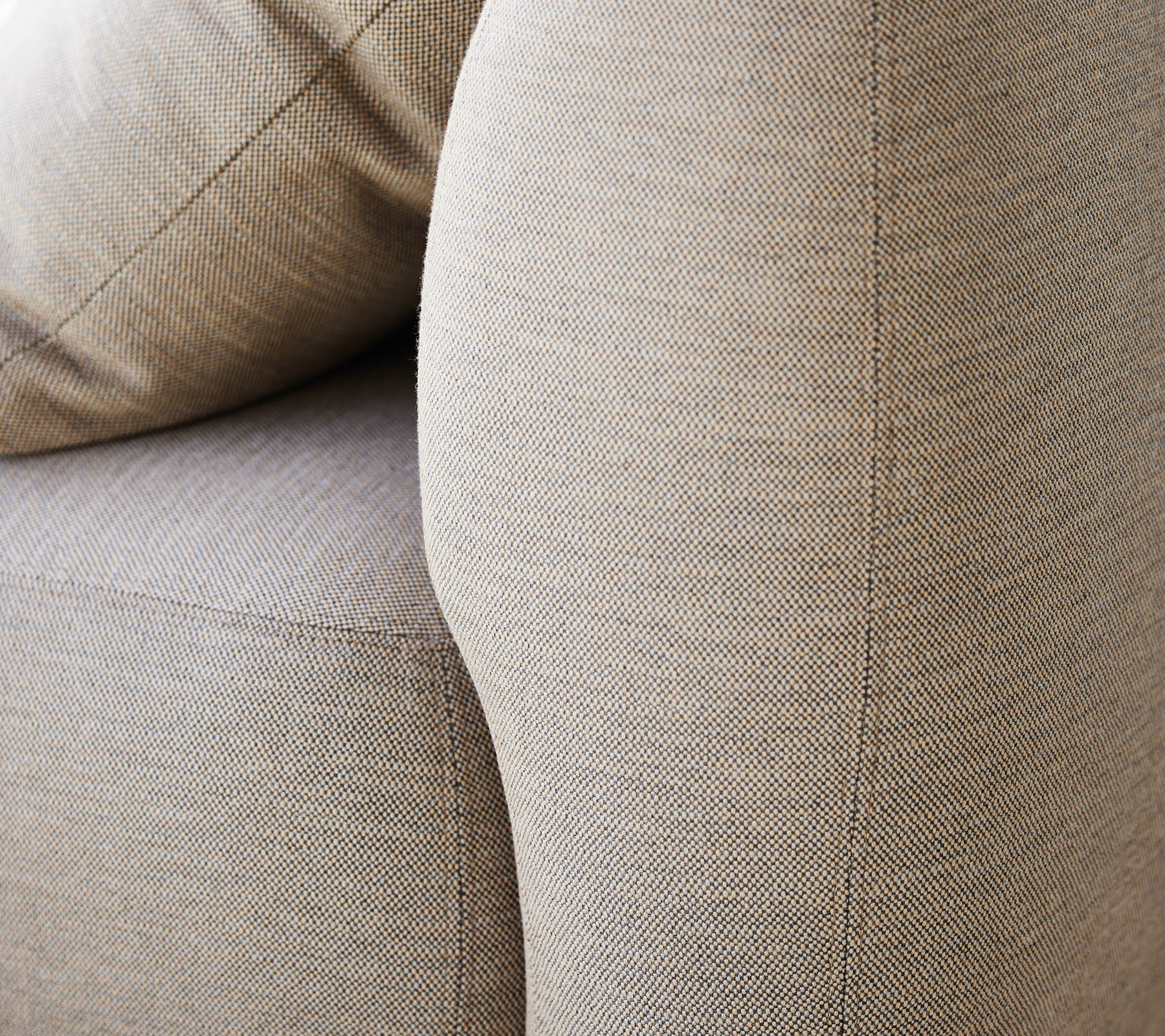 Nærbilde av et teksturert beige stoff, som fremhever det buede armlenet og de myke putene på et møbel.