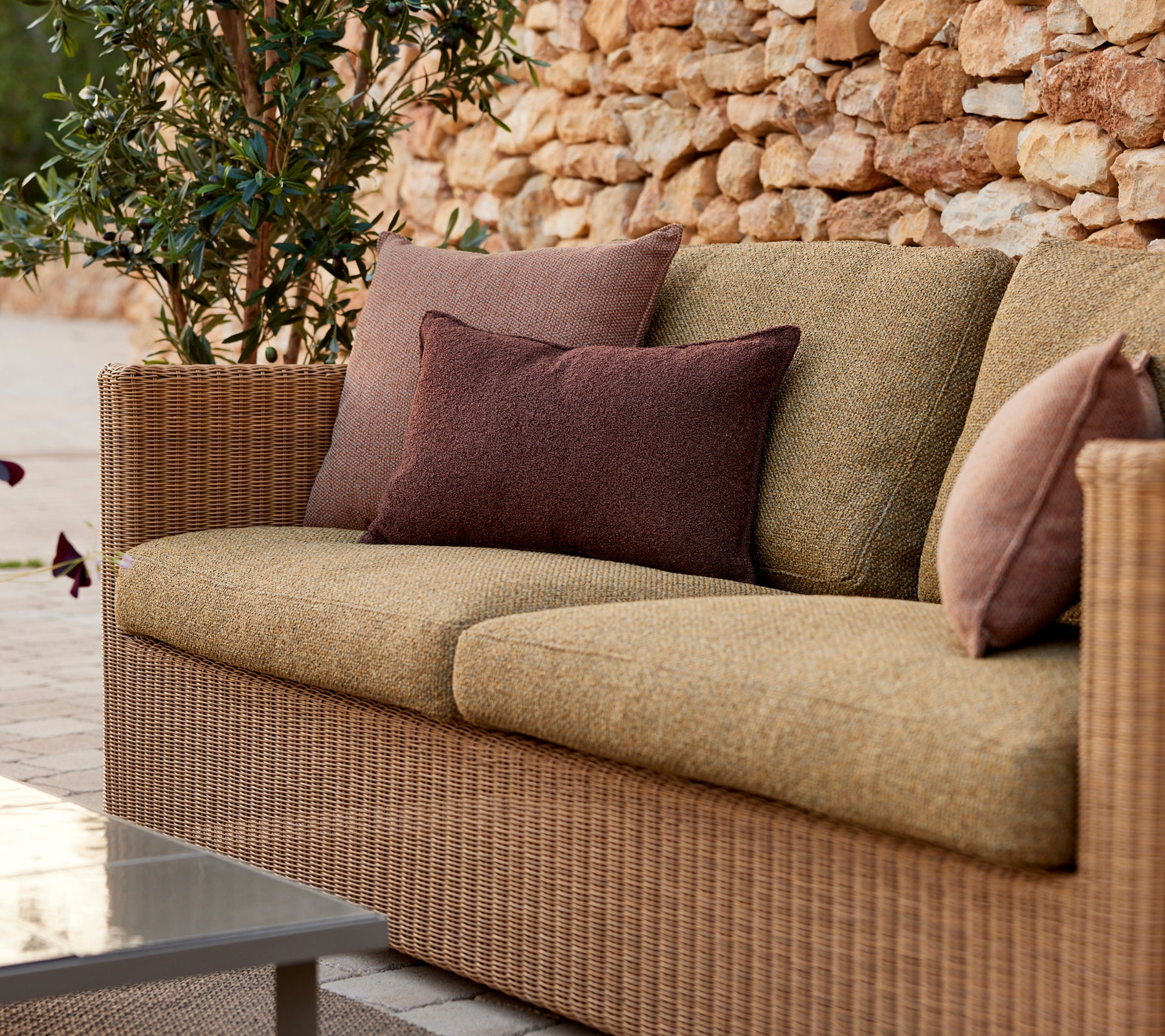 Moderne beige sofa med lilla og brune puter i en loungeinnstilling.