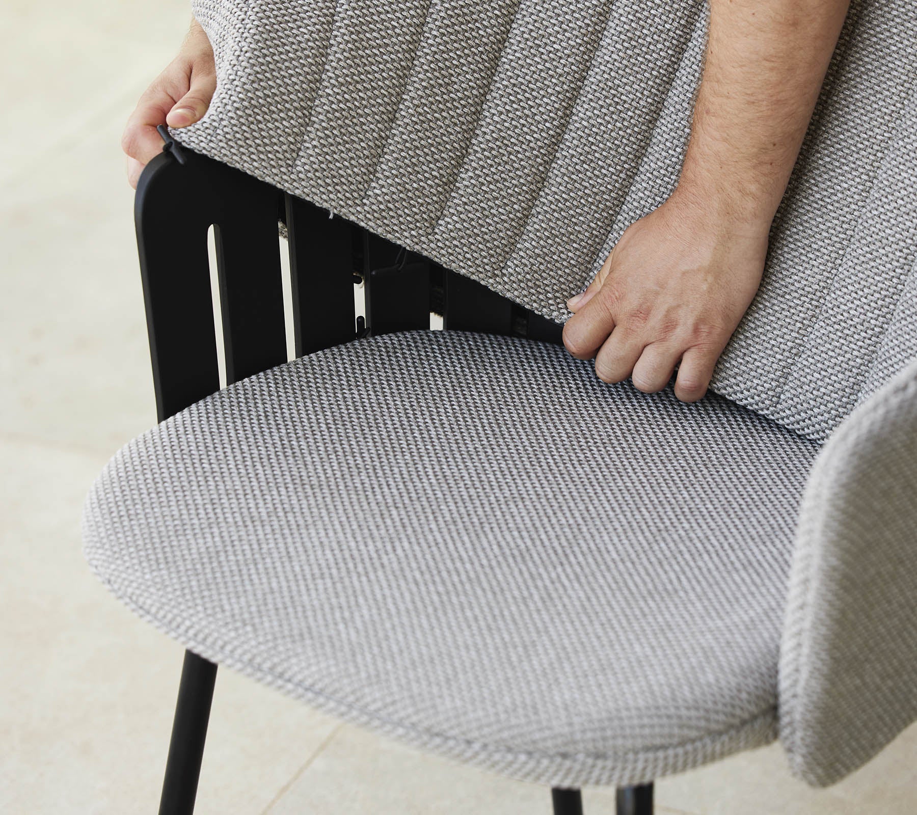 Person justerer ryggen på en moderne stol med et teksturert stoffsete, som viser et stilrent design og ergonomisk støtte.
