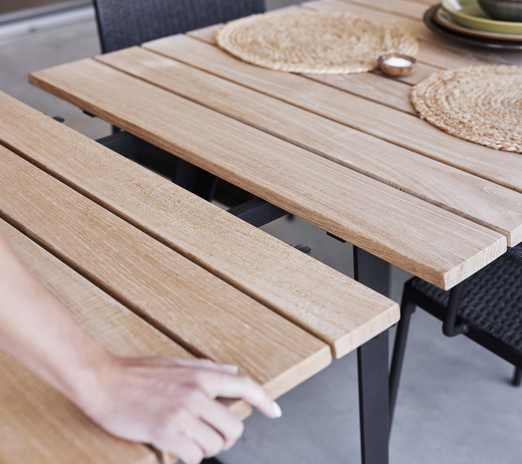 Detalj av et trebord med lamelldesign, bordbrikker og en minimalistisk estetikk, perfekt for bespisning eller sammenkomster.