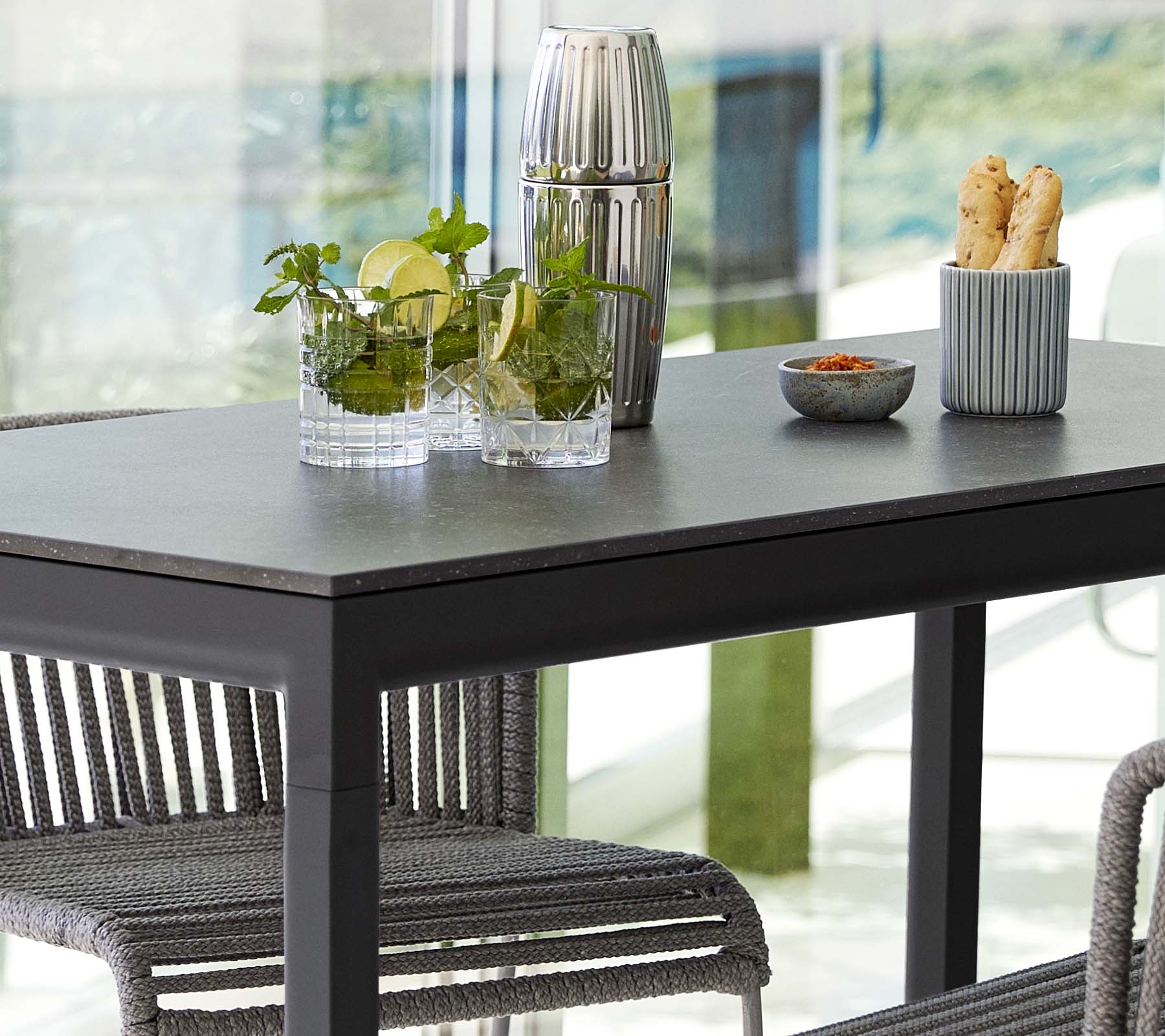Et moderne bord satt med planter i glassvaser, en dekorativ beholder og en skål med snacks, omgitt av stilige stoler.