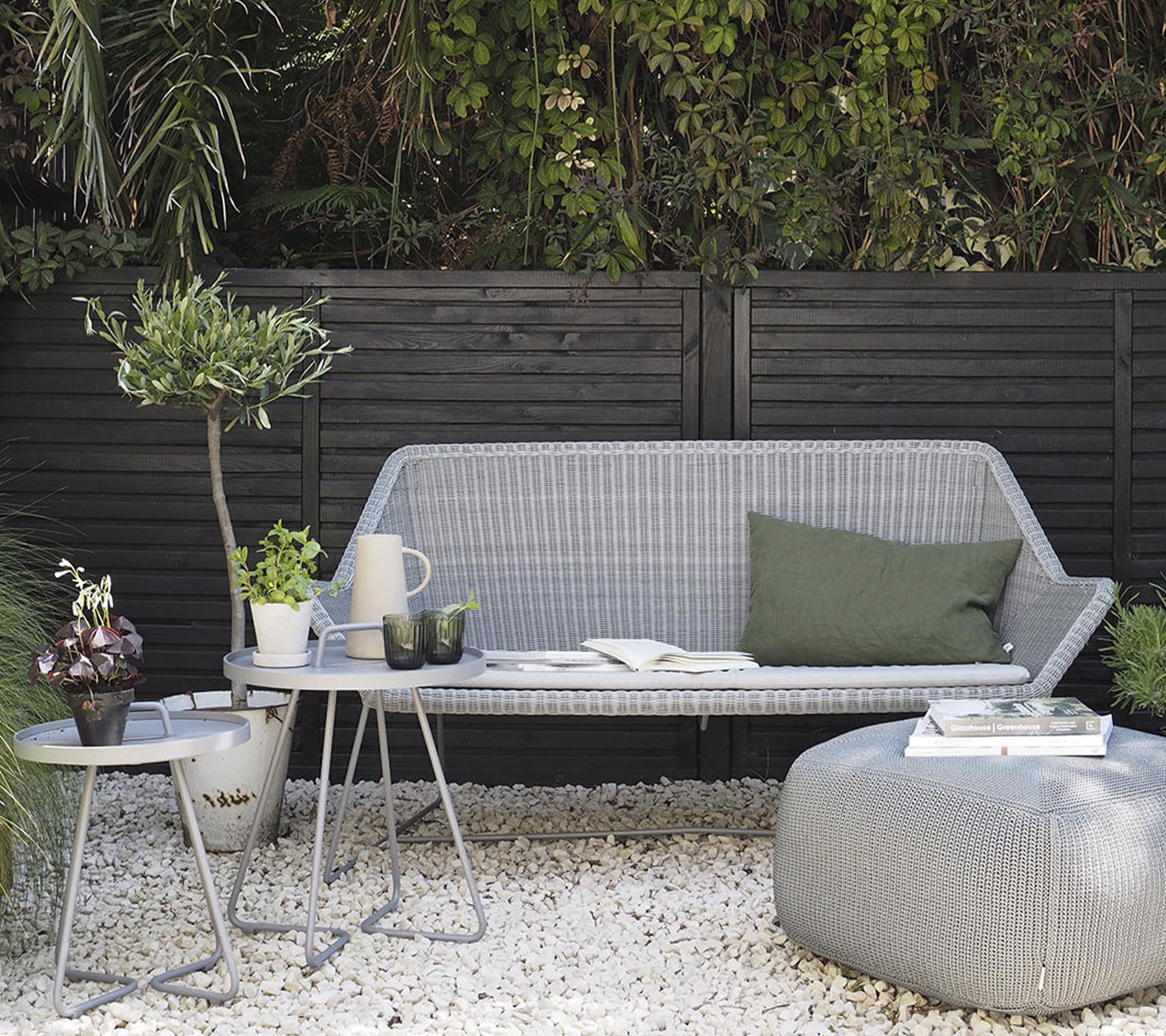 Minimalistisk utendørs møbeloppsett med en stilfull sofa, sidebord og dekorative planter på en grusoverflate.