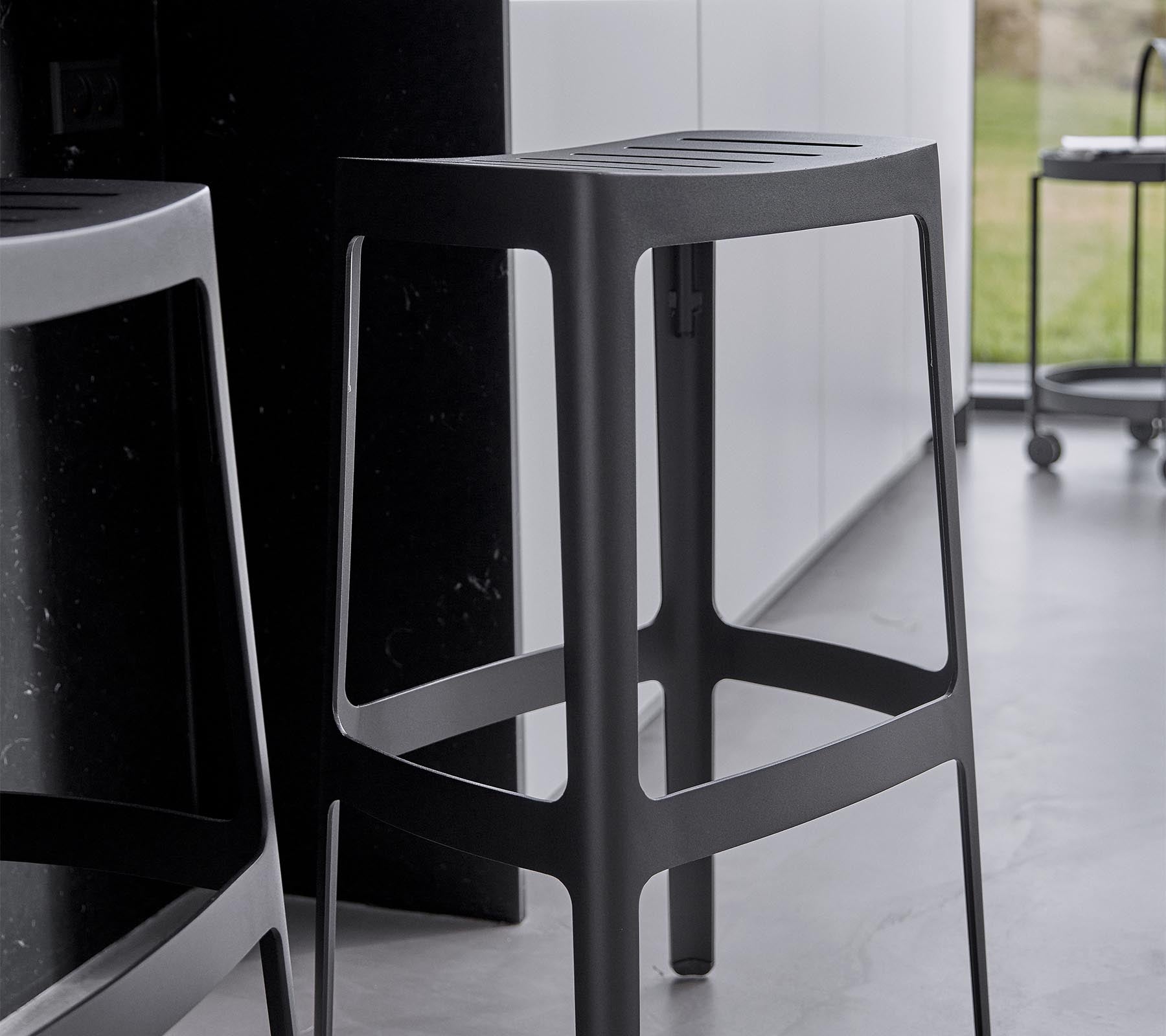 En slank, moderne barstol med et minimalistisk design, som har en robust struktur og en elegant svart finish.
