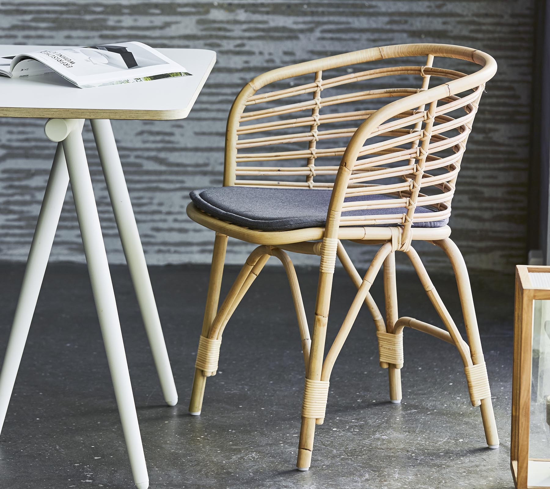Stilfull kurvstol med en grå pute, kombinert med et enkelt bord og moderne dekor. Passer til uformelle sitteplasser og avslapning.