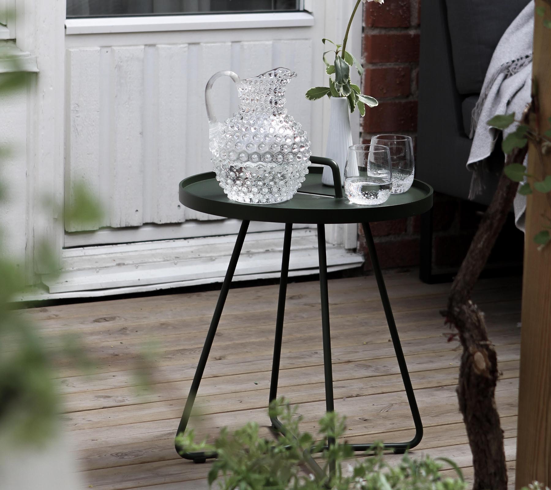 Et stilfullt grønt sidebord med en krystallkaraffel og to glass, komplettert med frisk grønt i området.