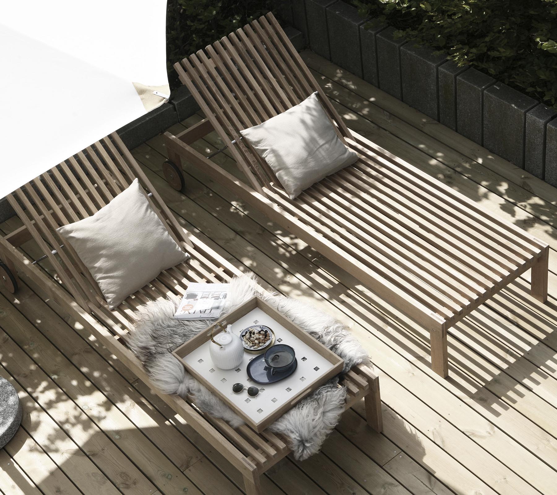 To tre-lounge stoler med puter er plassert ved siden av et lite bord dekorert med et koselig teppe og dekorative gjenstander. Naturlig lys filtrerer gjennom.