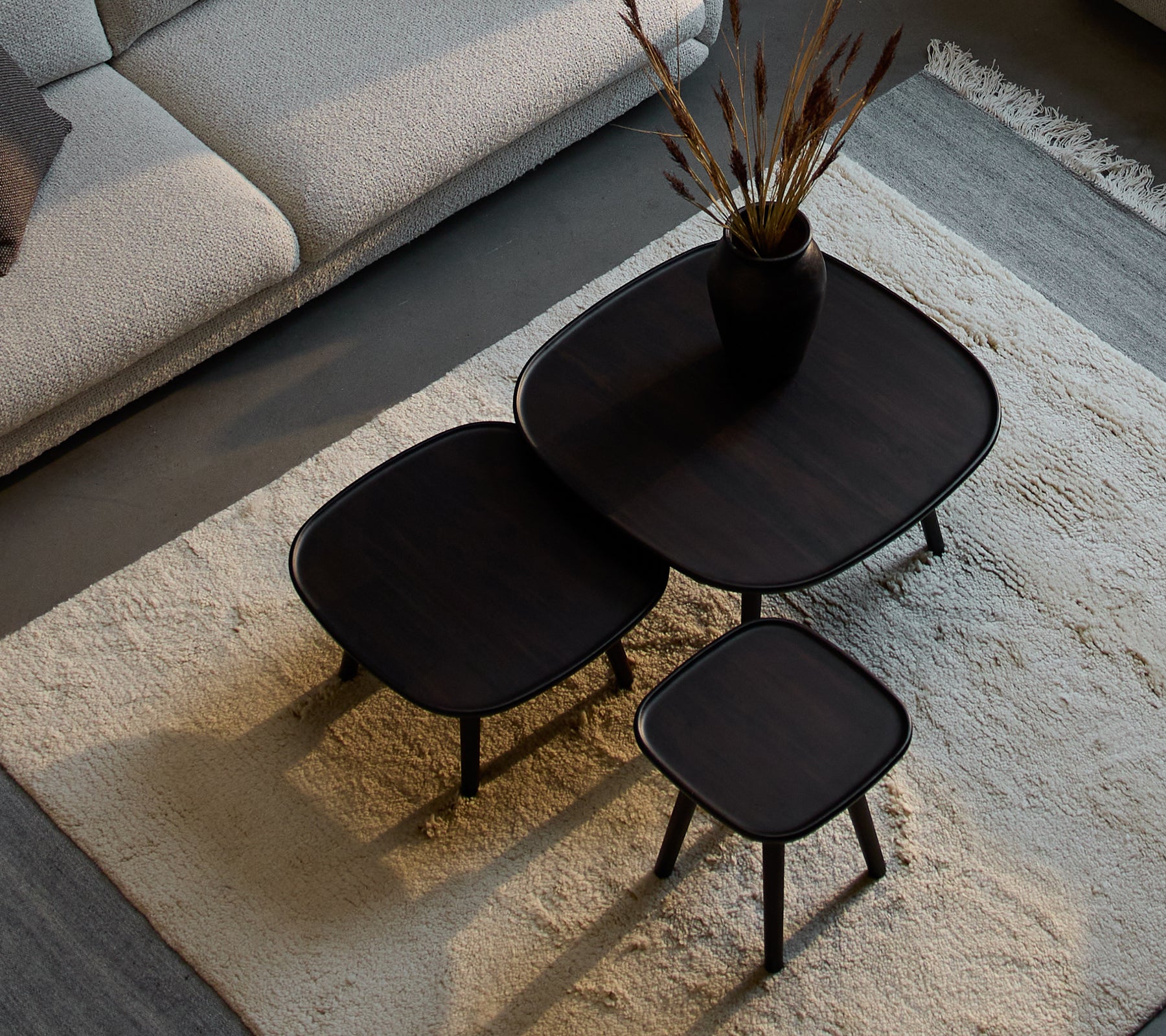 Tre stilige Pace kaffebord i forskjellige størrelser, med et stilrent design og mørk finish, ledsaget av en dekorativ vase og tørkede planter.