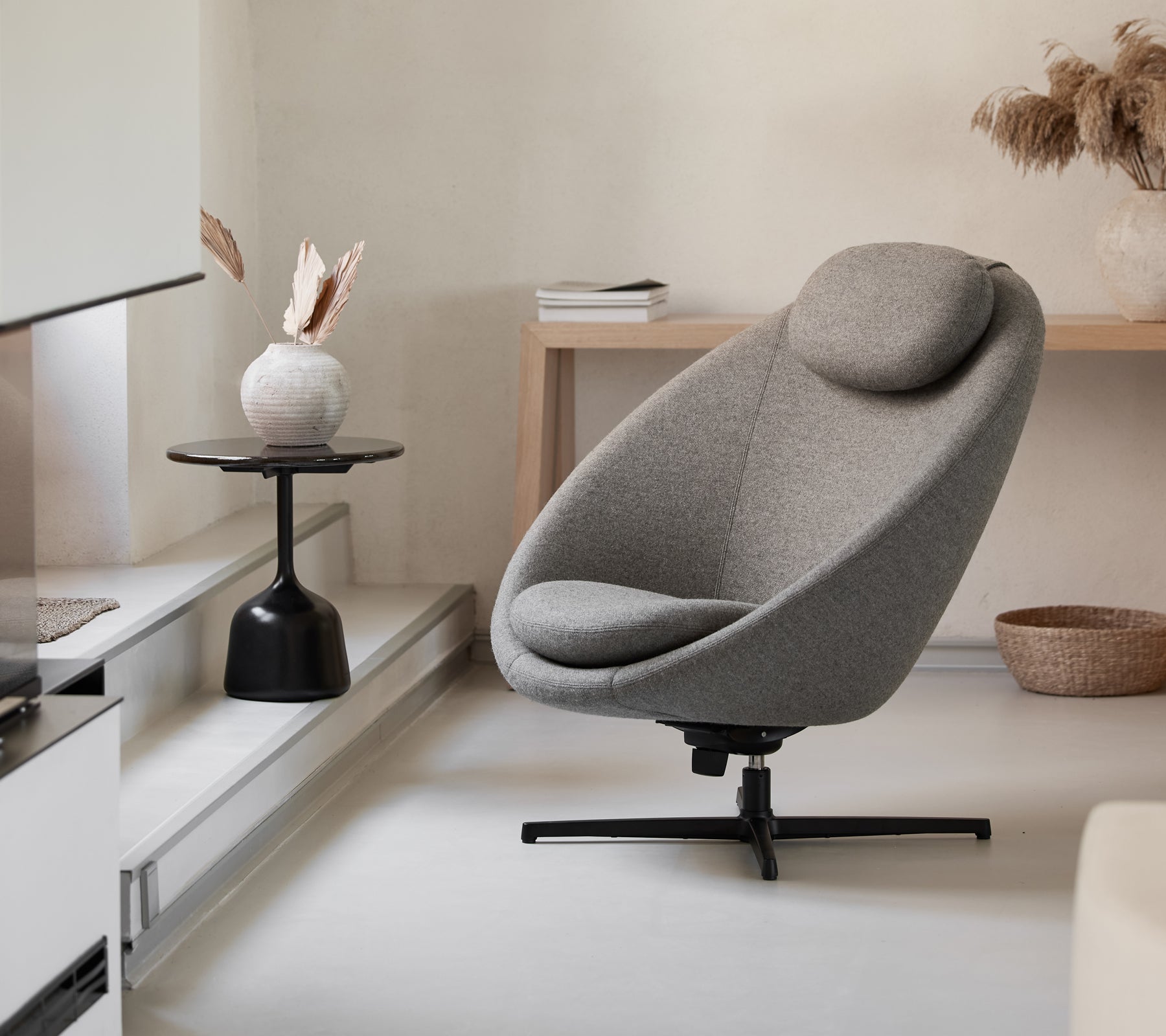 Stilig grå stol med en bølget form og støttende hodepute, komplettert med et minimalistisk sidebord og dekorative elementer.