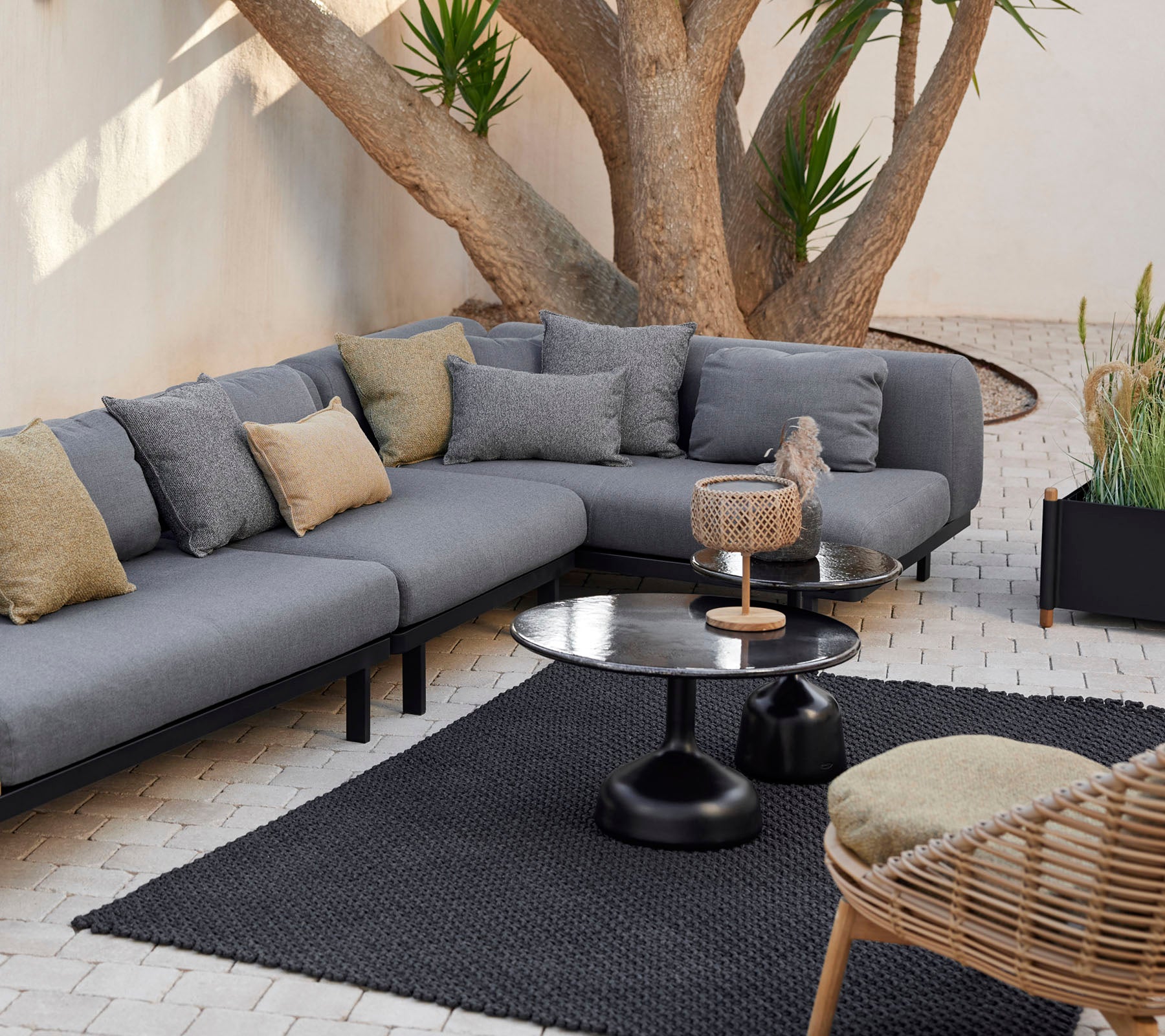 Loungeområde med en grå modulsofa med dekorative puter, et stilrent kaffebord og et teksturert teppe omgitt av grønt.