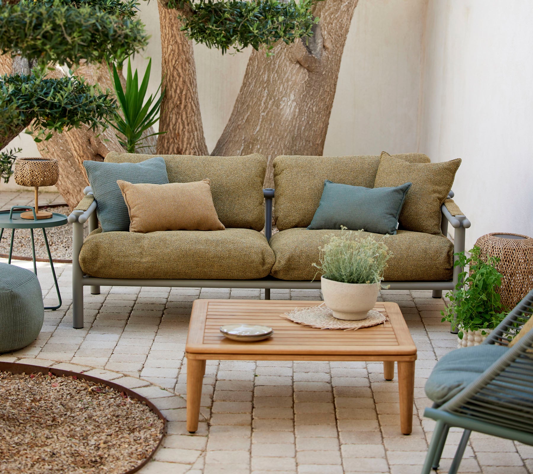 Behagelig sitteområde med en grønn sofa med puter, et trekaffebord og dekorative planter i en rolig setting.