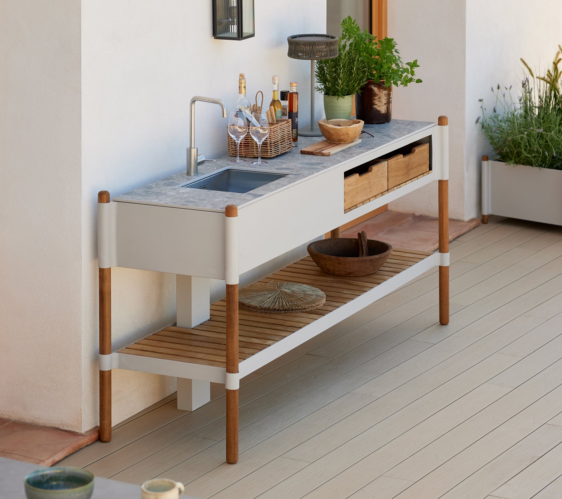 En moderne, minimalistisk utendørs vaske stasjon med granittopp, trelagringsskuffer og dekorative planteoppsett.