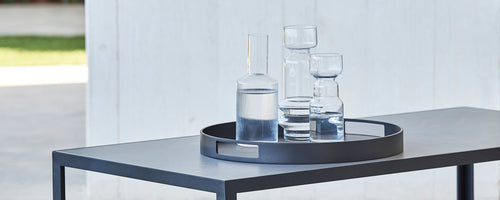 Et rundt serveringsbrett som holder forskjellige glassvarer, inkludert en høy mugge og flere glass, plassert på et strømlinjeformet bord.