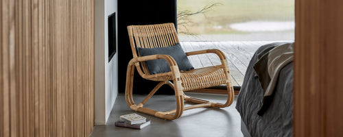 Woven chair with a comfortable cushion, positioned beside a bed, showcasing a modern and stylish design in a serene setting.