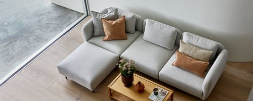 En stilfull lys grå sofa med koselige puter, supplert med et trebord og en liten potteplante.